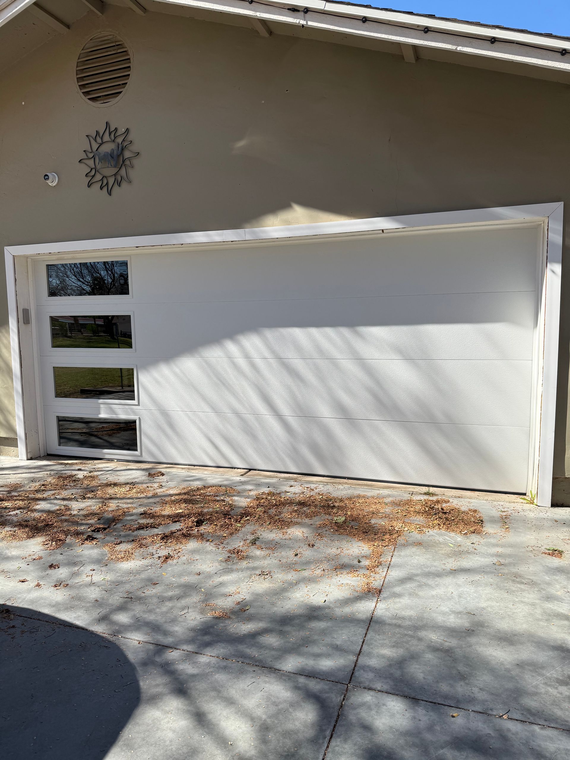 White garage door with a vertical row of four windows on the left side, set against a house exterior with scattered leaves.
