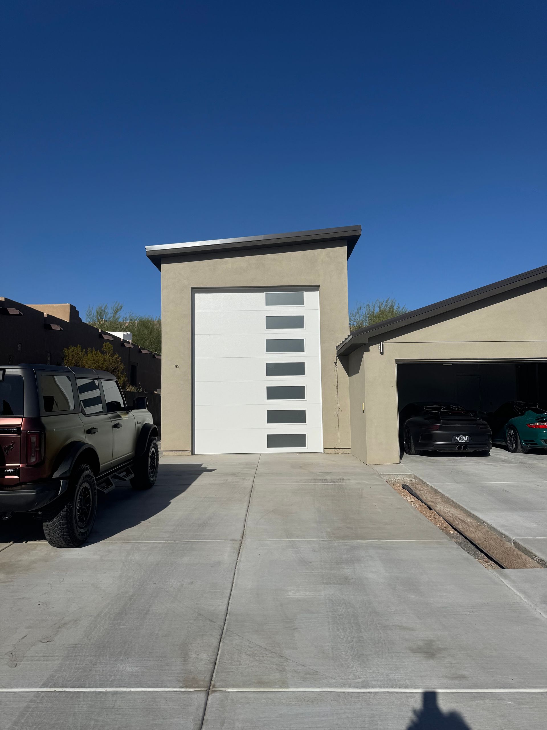 An exterior view of a modern garage with a white, side-lit door next to a standard parking space under a blue sky.