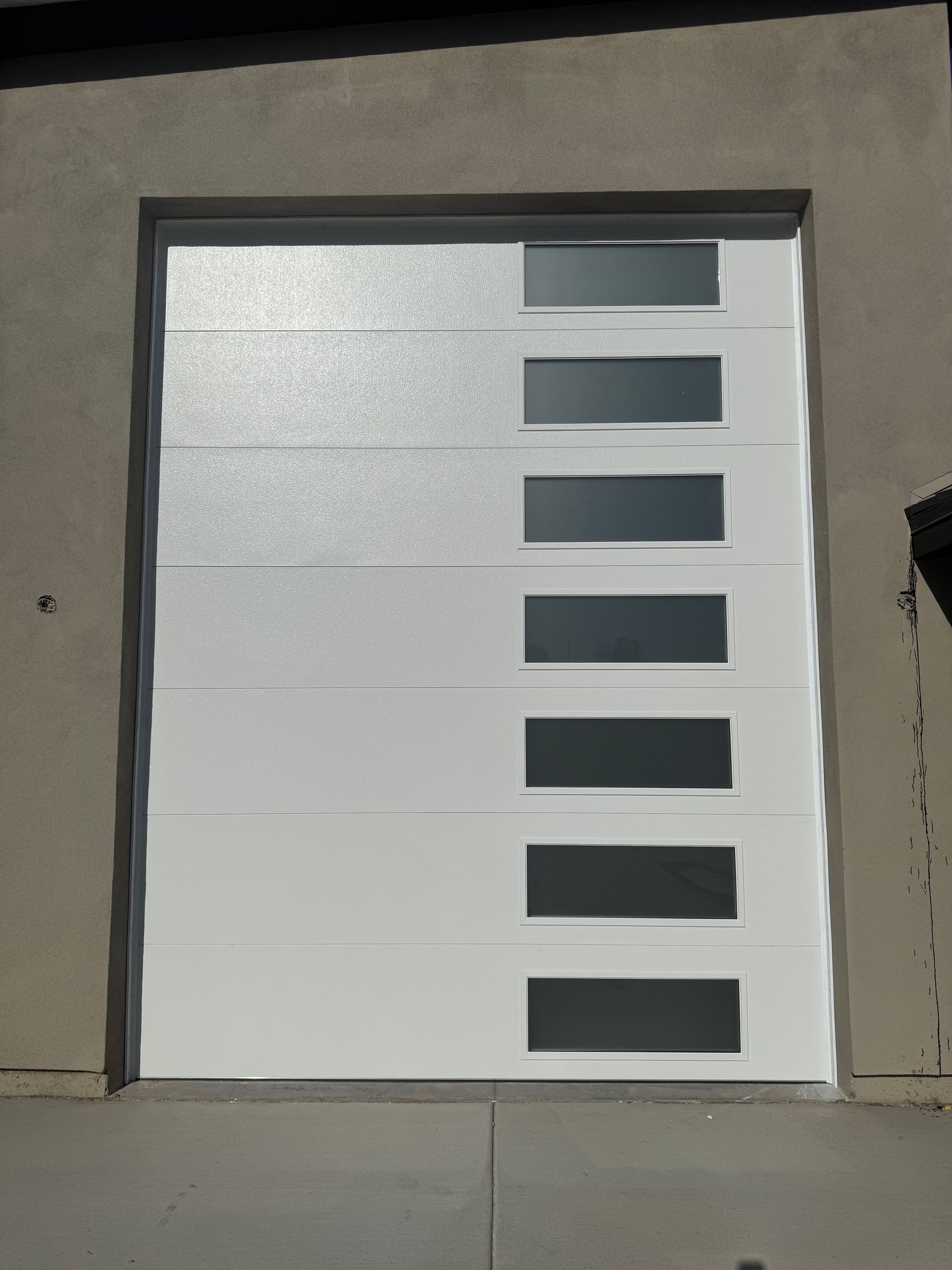 White modern garage door with a vertical row of six rectangular frosted glass windows on the right side.
