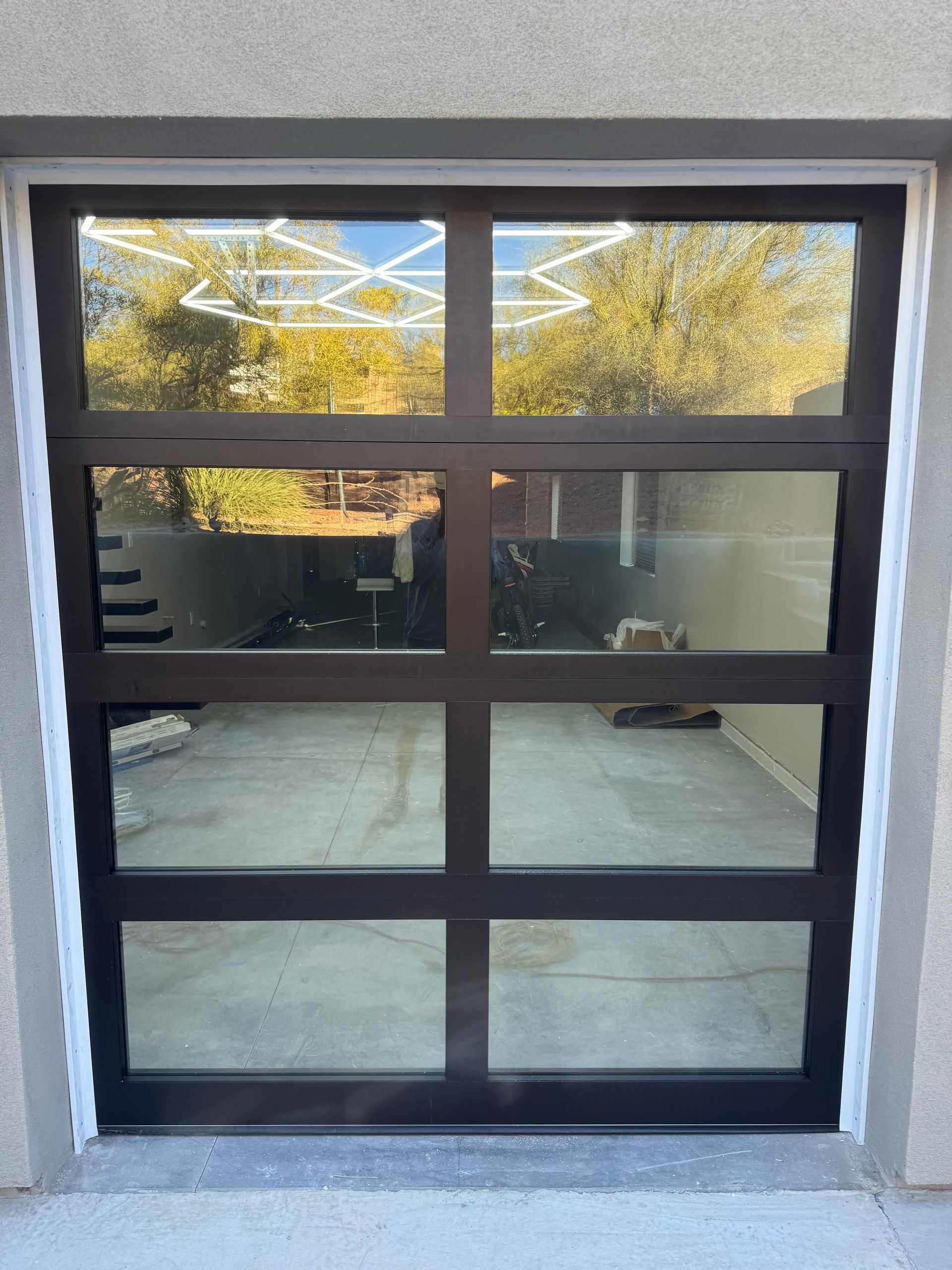 A dark-framed, modern glass garage door with four horizontal rows of rectangular windows, set into a light-colored wall.