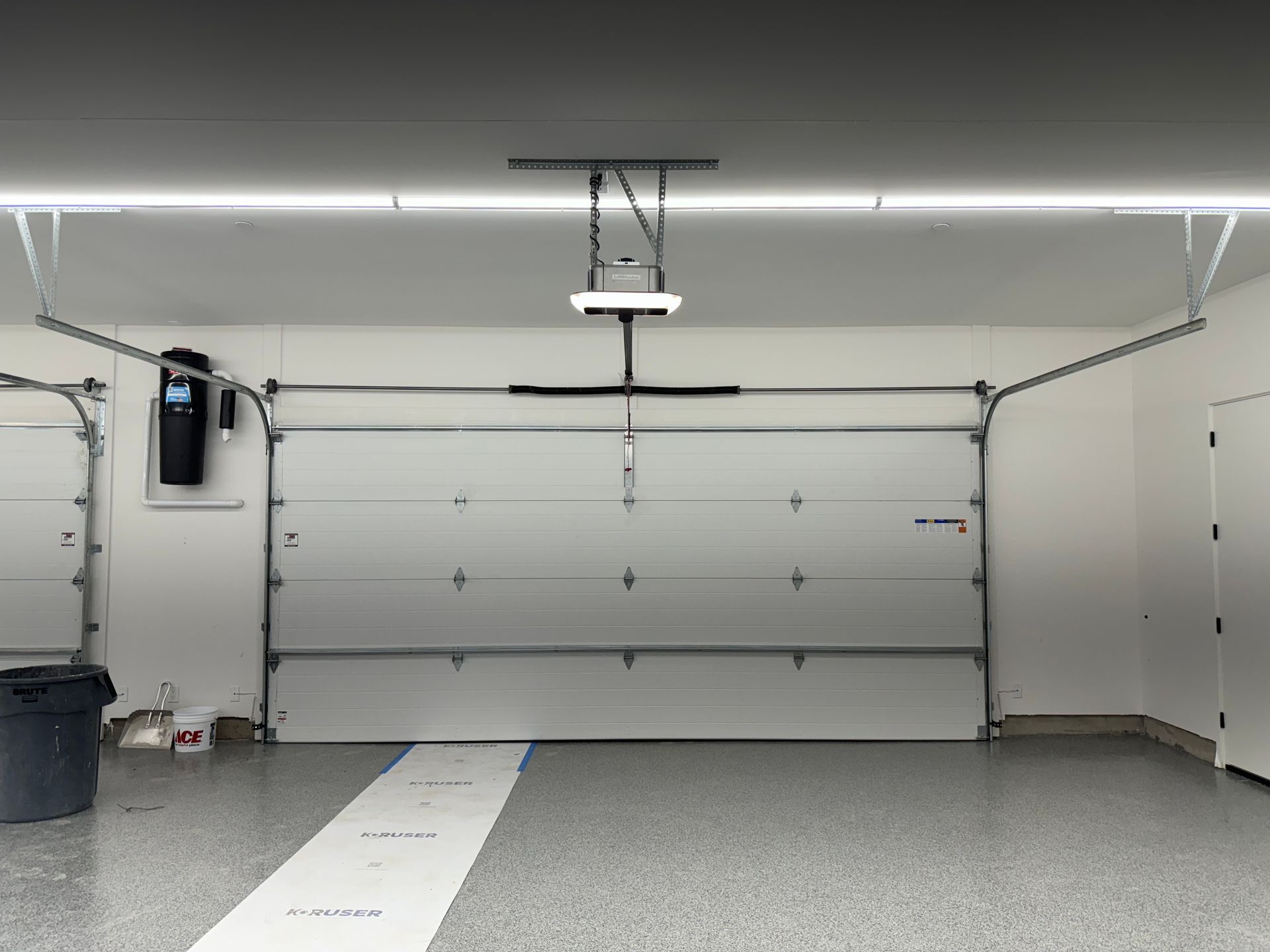 An interior view of a clean, well-lit garage with a closed white sectional garage door and a speckled epoxy floor.