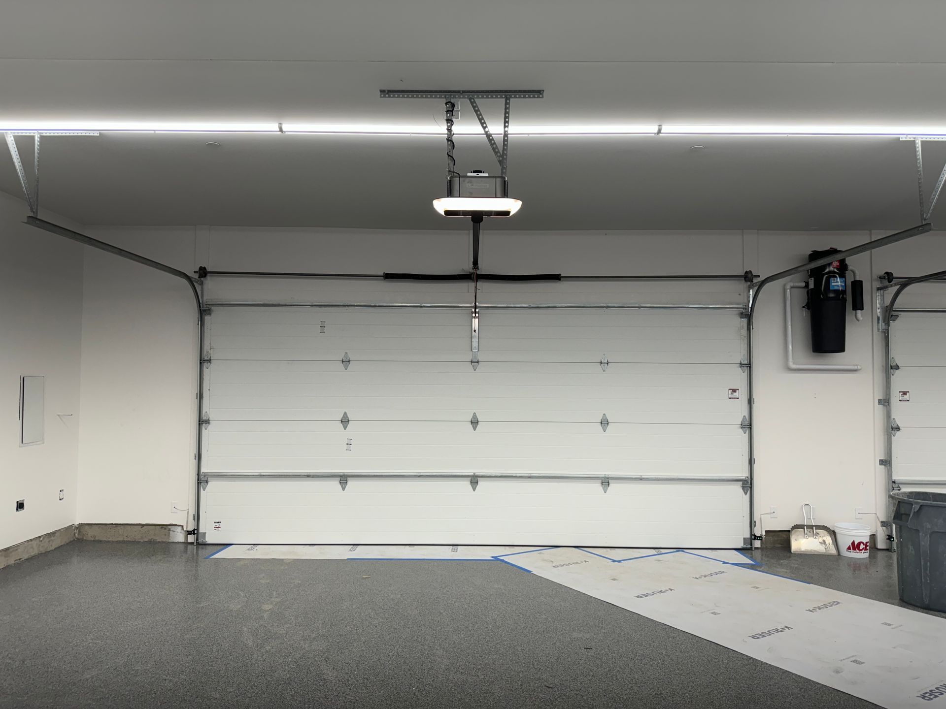 A modern, clean garage interior featuring a closed white sectional garage door and a ceiling-mounted automatic opener.
