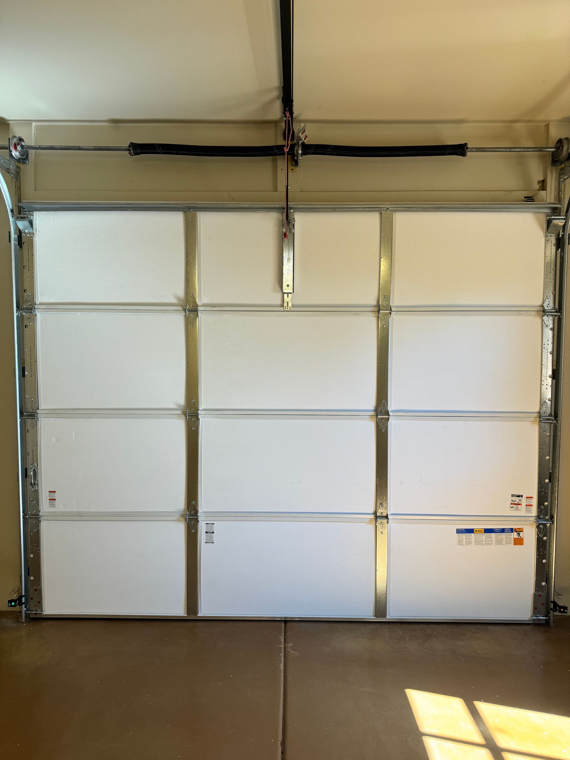 Interior view of a white, paneled sectional garage door with metal frames and a spring mechanism at the top.