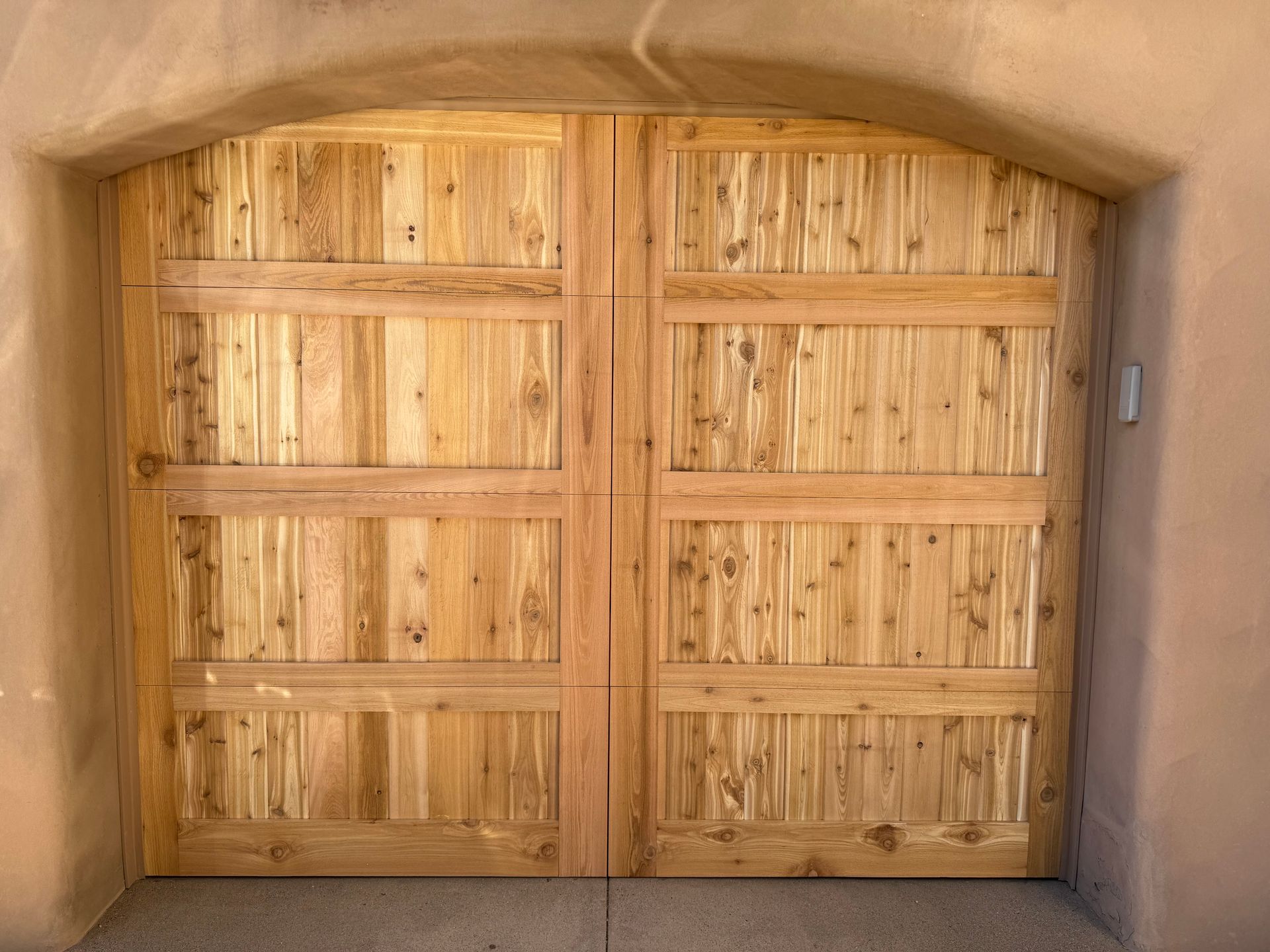 Double wooden garage doors with horizontal paneling set within a rounded, textured adobe-style archway.