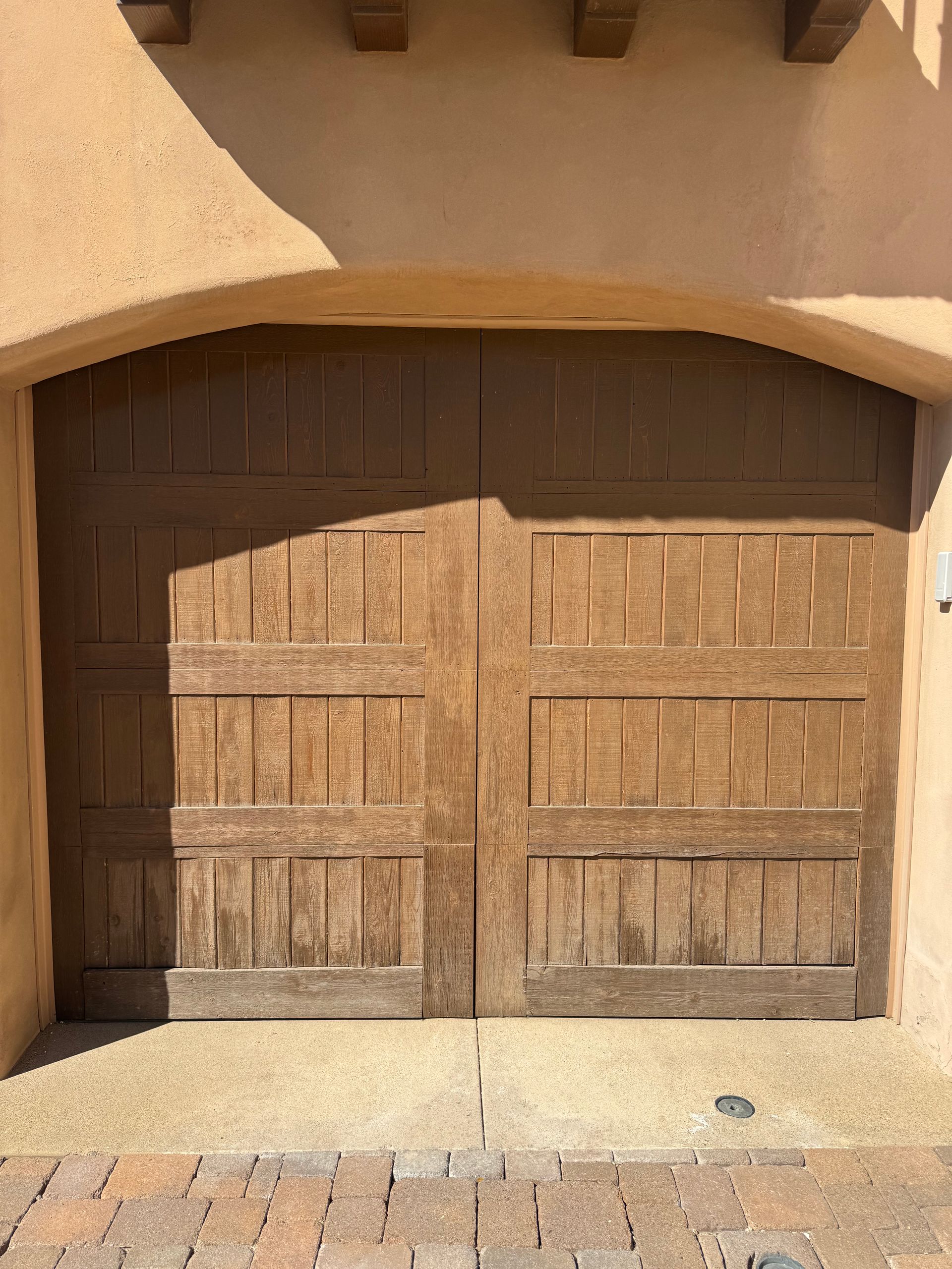 A rustic, dark brown wooden garage door with vertical panels set under a stucco archway.