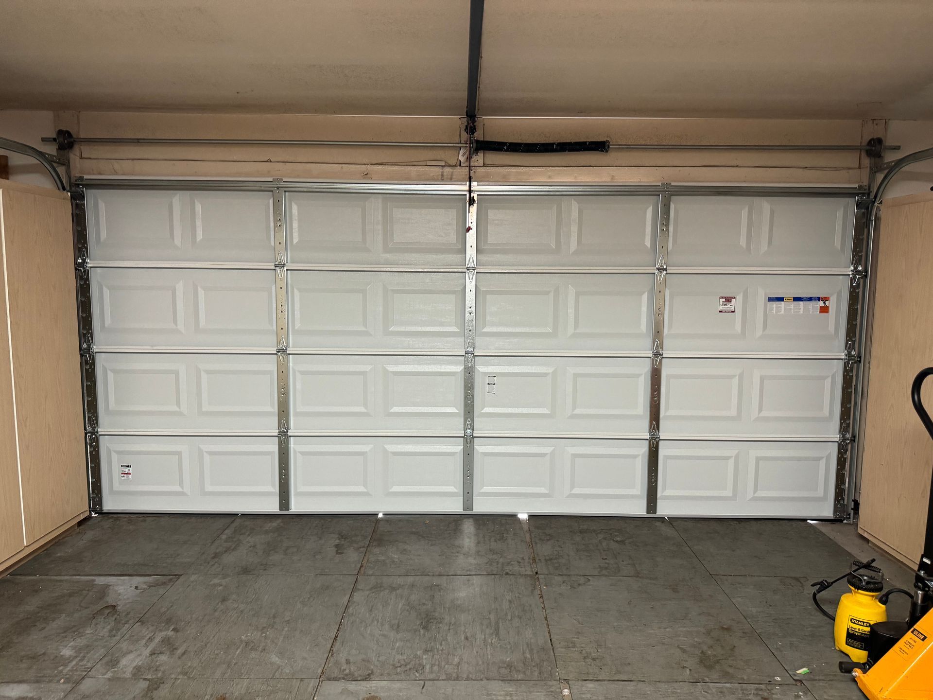 A white, four-panel residential garage door viewed from inside a garage with concrete flooring.