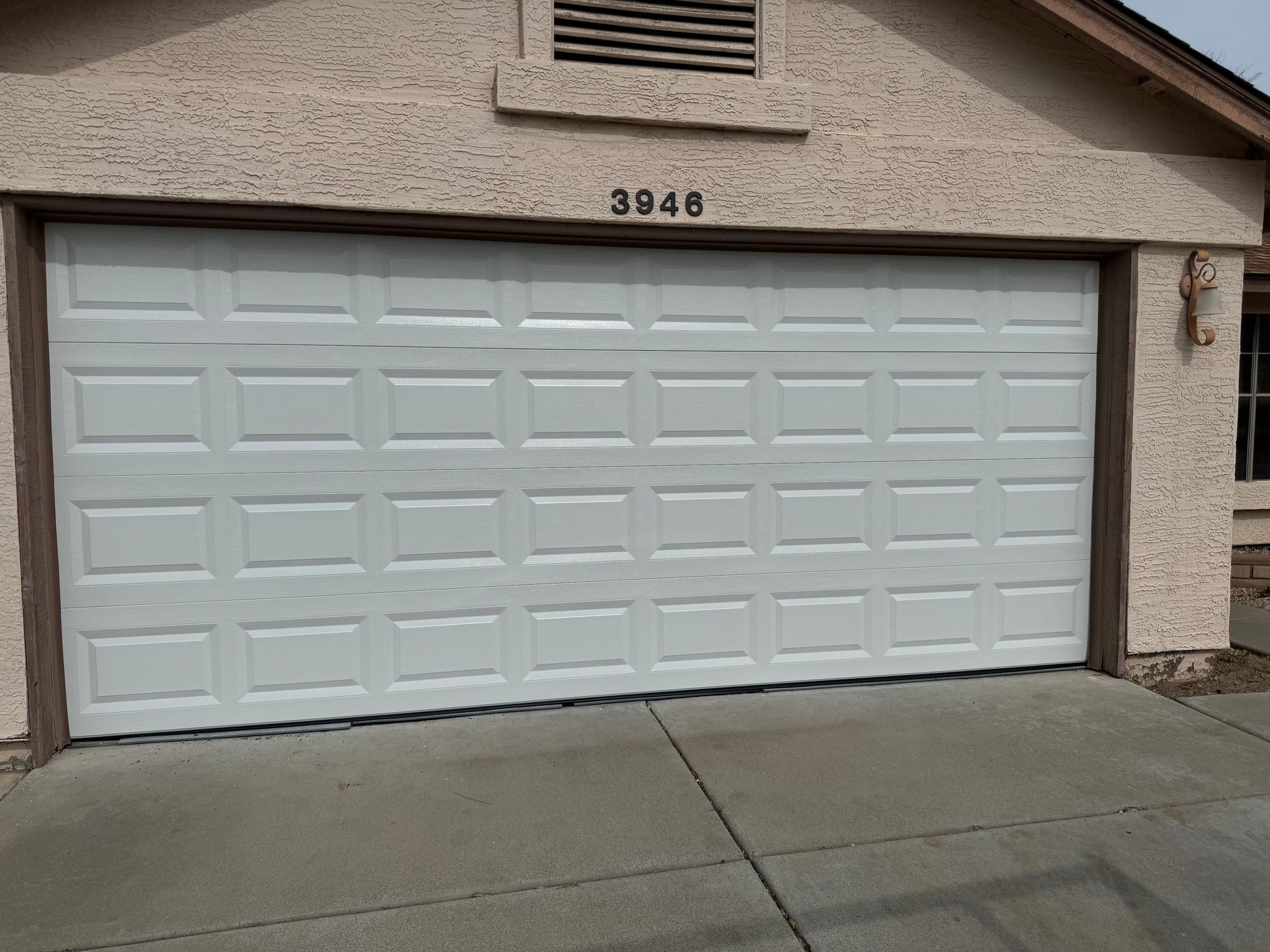 A white, rectangular garage door with raised panels and the address number 3946 above it, set in a tan, stucco house.