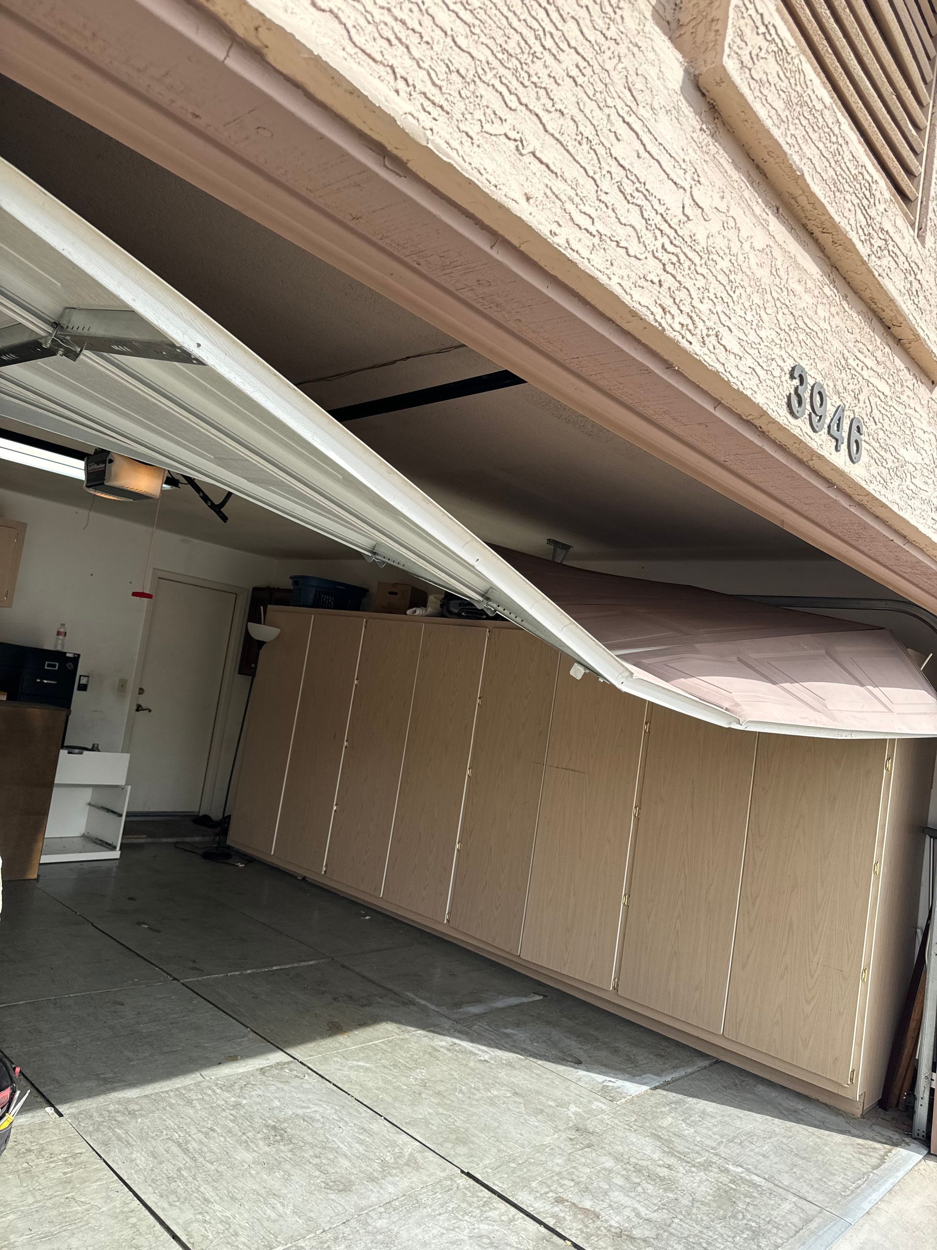 A damaged garage door is partially collapsed and hanging off its track, revealing the interior of a residential garage.