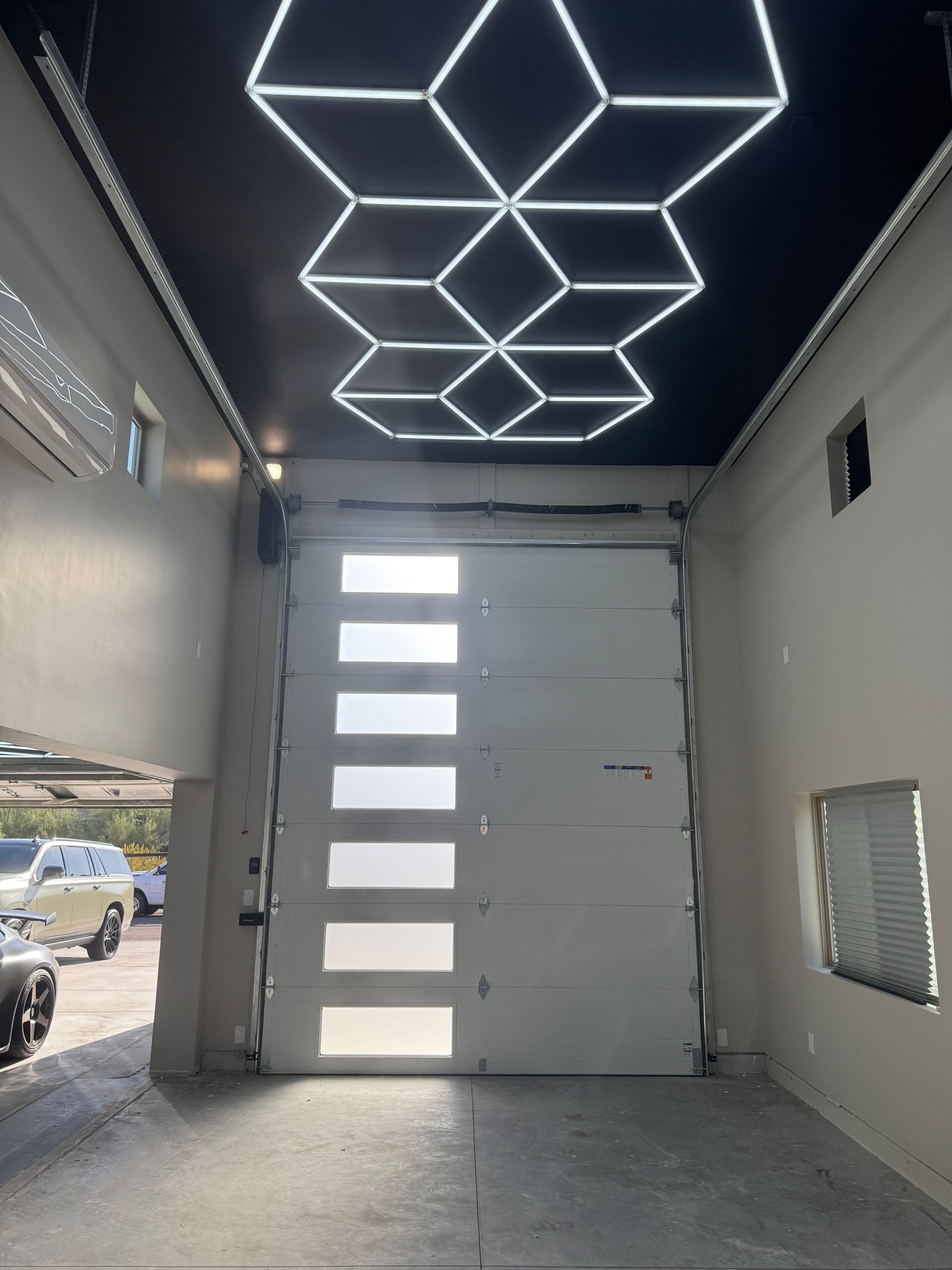 A garage interior featuring a white sectional door with horizontal windows and a geometric LED light pattern on the ceiling.