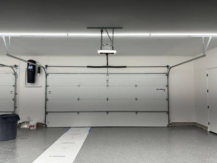 Interior view of a garage with a closed white sectional door, an overhead opener, and speckled gray epoxy flooring.