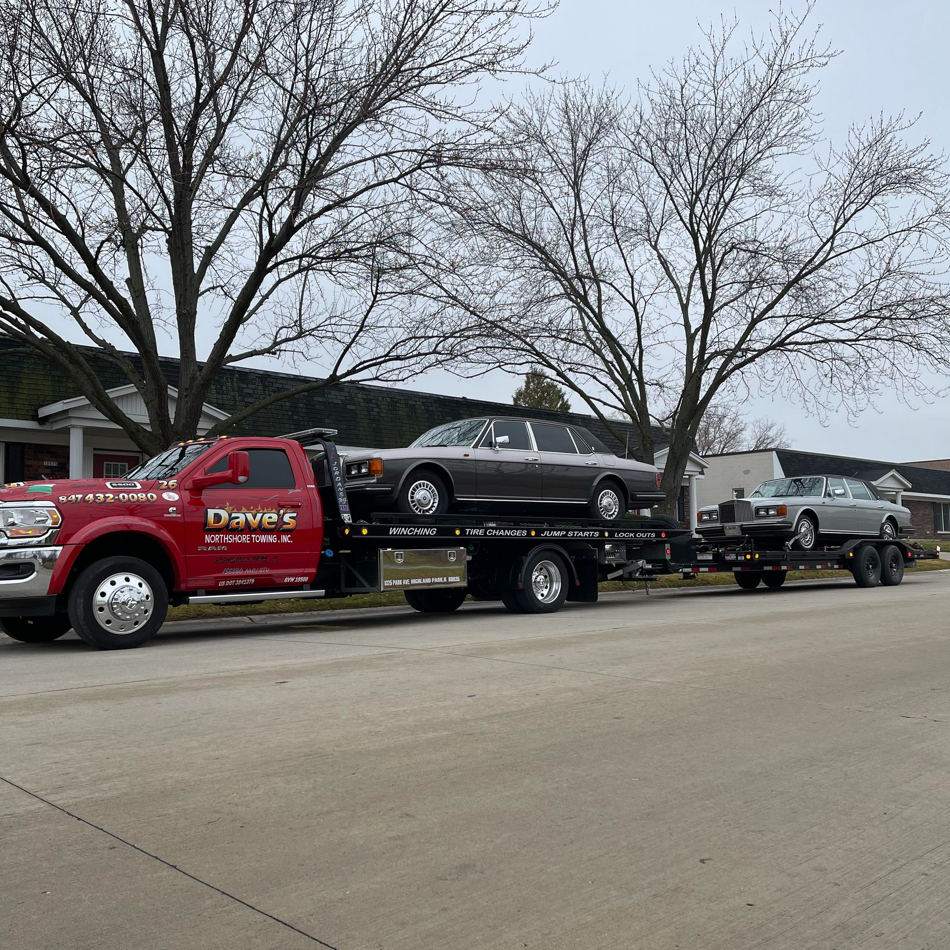 A red tow truck is carrying two cars on a trailer.