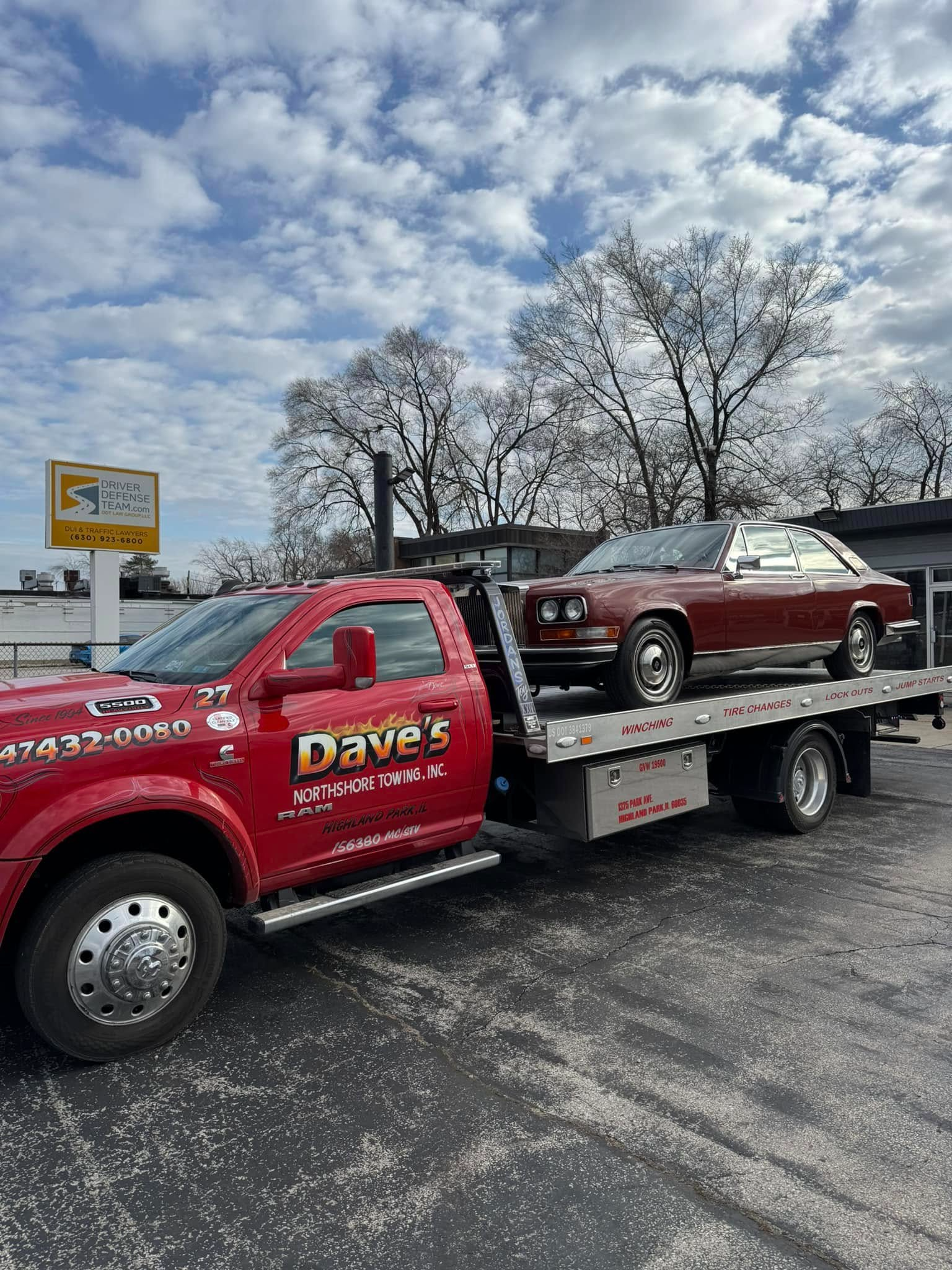 A red tow truck is towing a red car in a parking lot.
