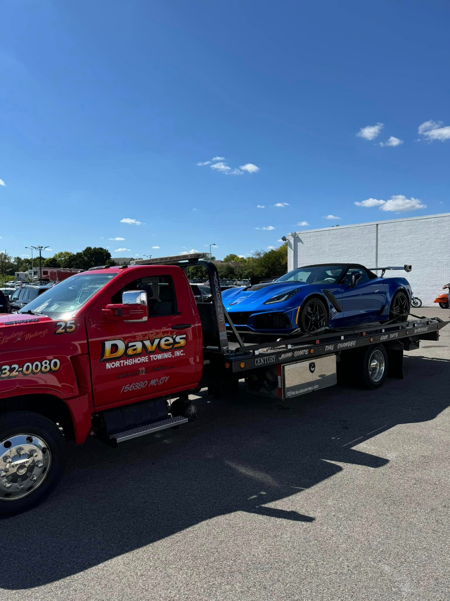 A red tow truck is towing a blue sports car.