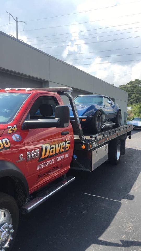 A red tow truck is towing a blue car.
