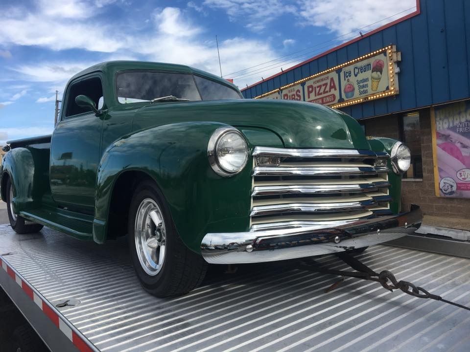 An old green truck is sitting on top of a tow truck.