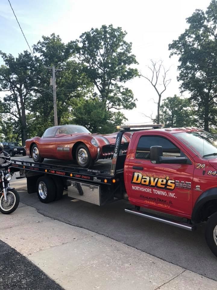 A red tow truck is carrying a red car and a motorcycle.