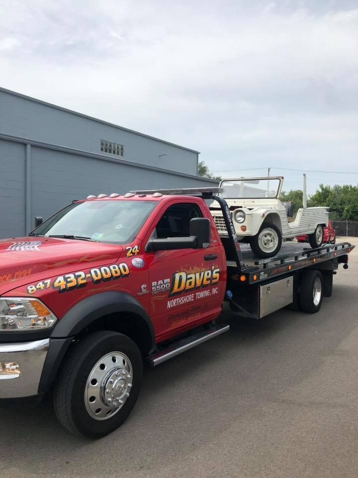 A red tow truck is towing a white jeep.