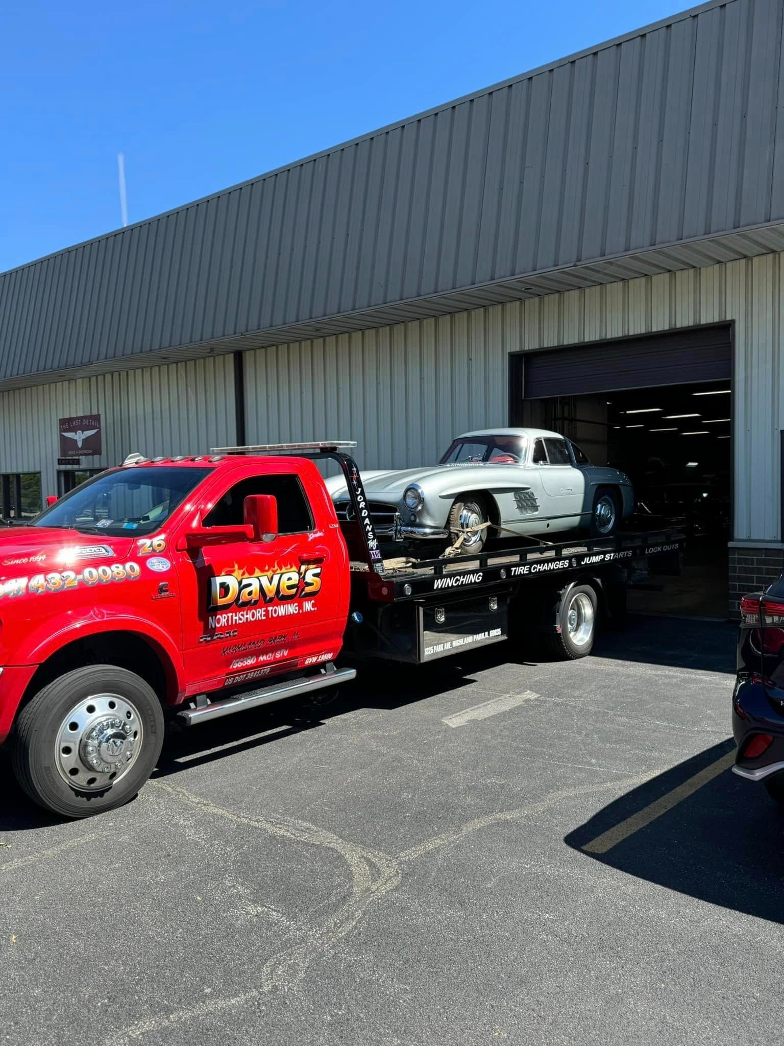 A red tow truck is towing a car in front of a building.