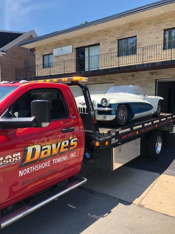A red tow truck is towing a car in front of a building.