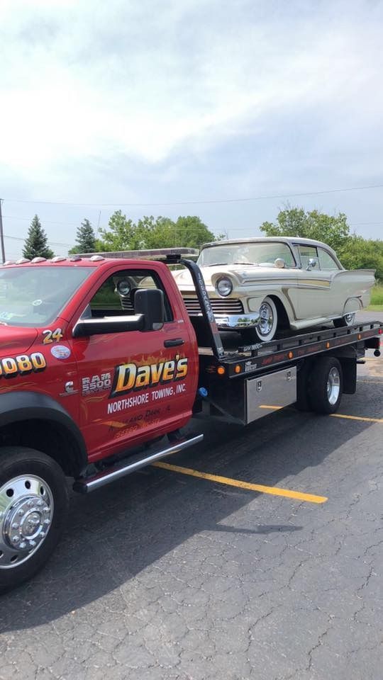 A red tow truck is towing a white car in a parking lot.