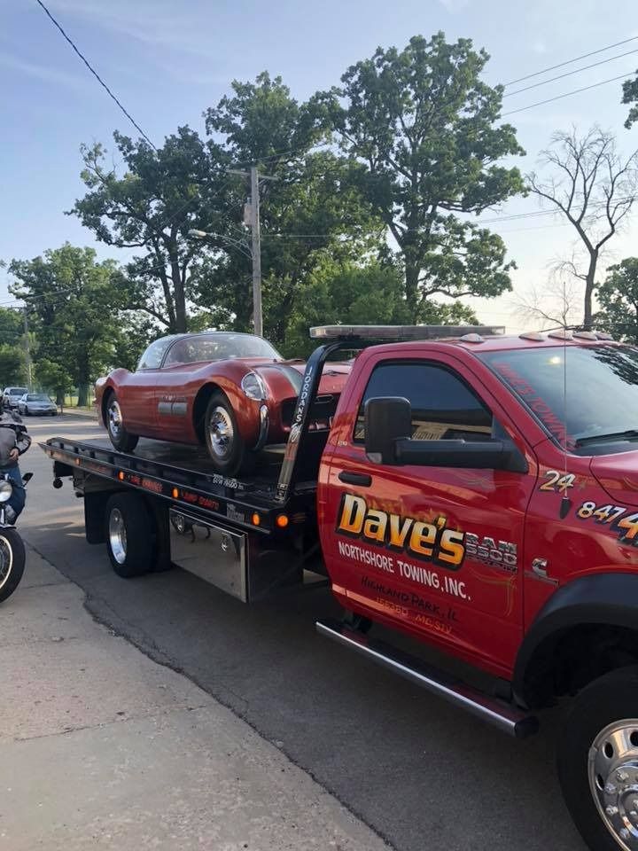 A red tow truck is carrying a car on the back of it.