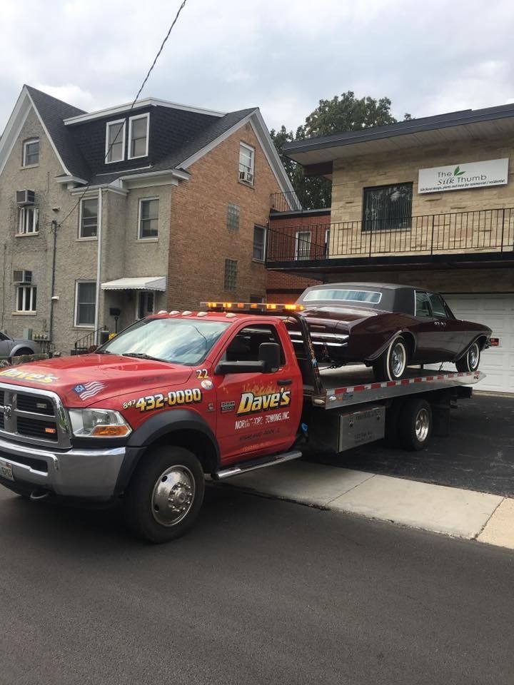 A red tow truck with a car on the back is parked in front of a house.