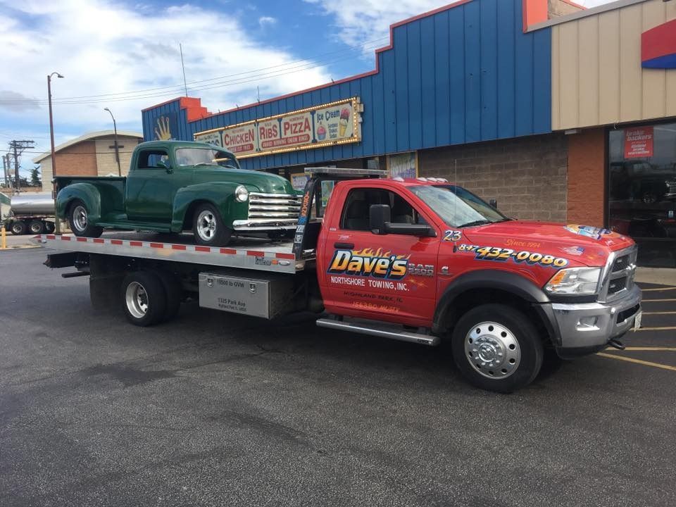 A red tow truck is towing a green truck.