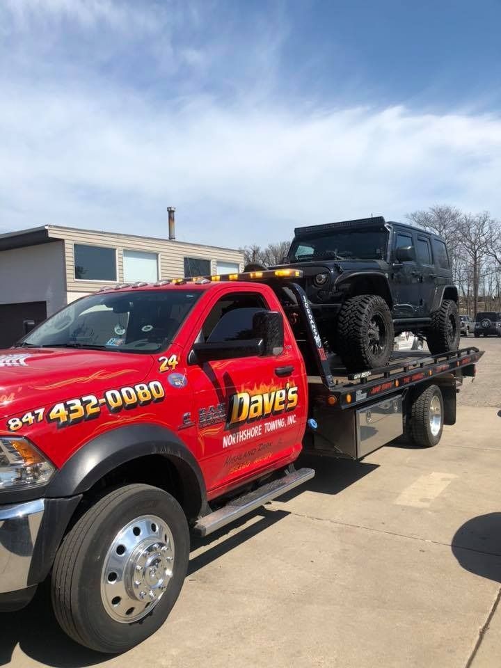 A red tow truck is towing a black jeep.