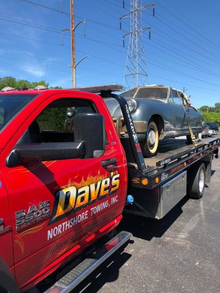 A red tow truck is carrying a car on the back of it.
