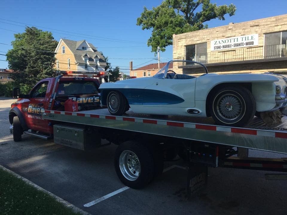 A white car is being towed by a tow truck.