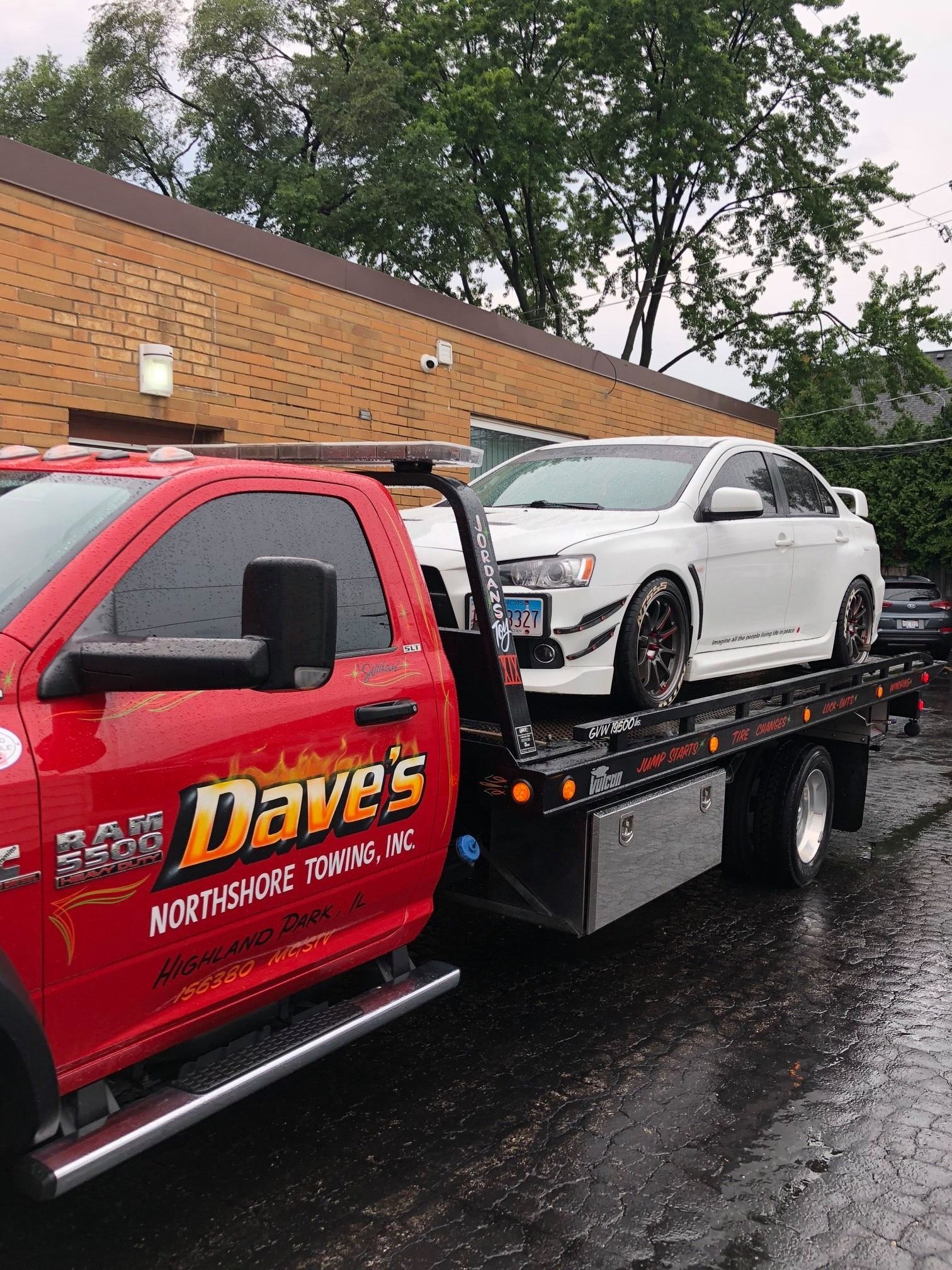 A red tow truck is towing a white car.
