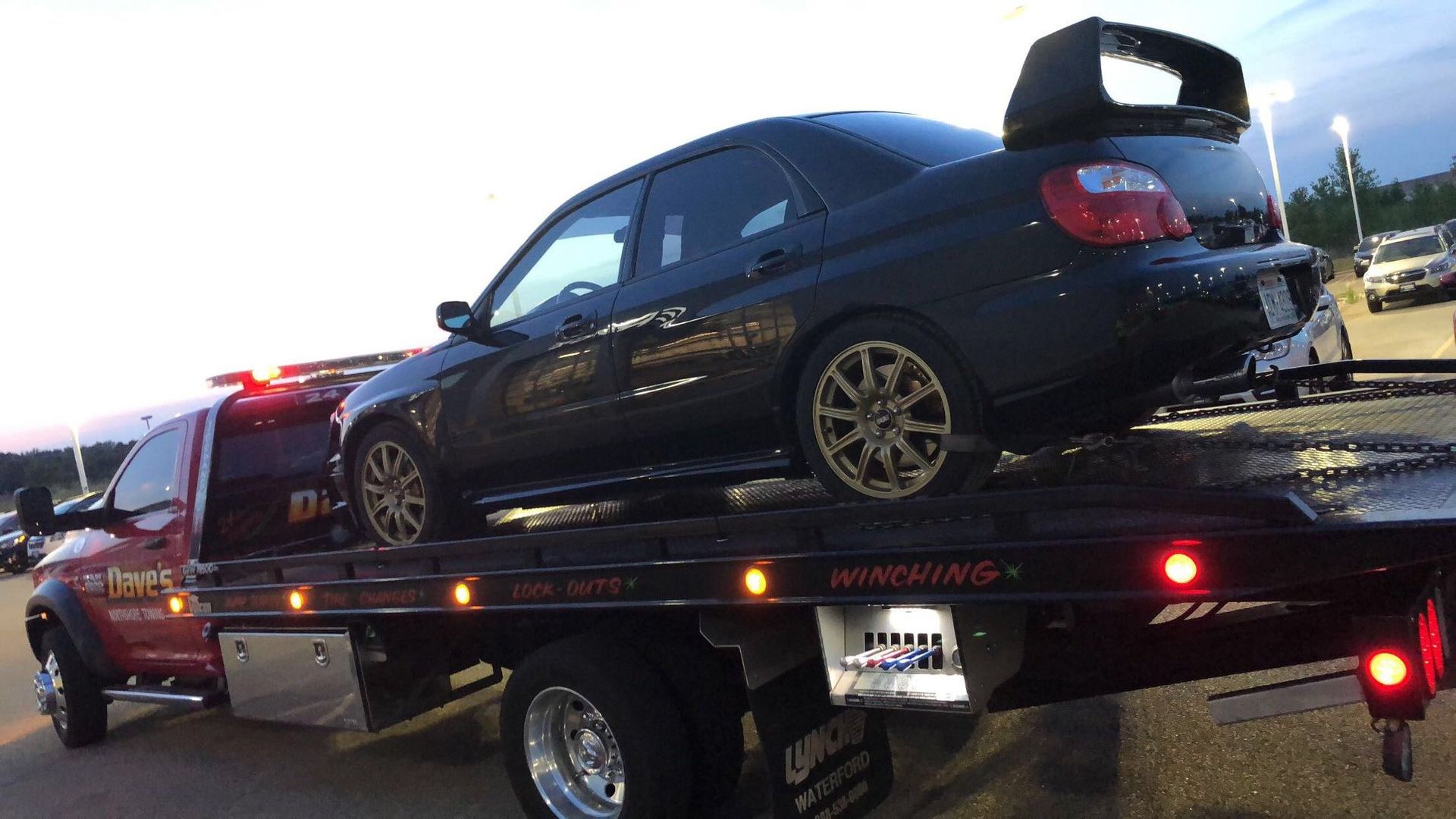 A black car is being towed by a tow truck.