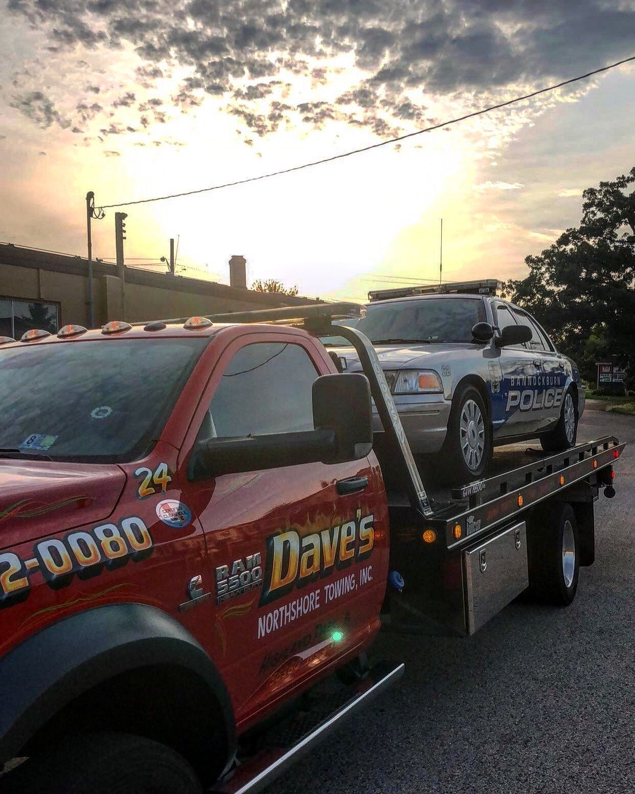 A red tow truck with a police car on the back of it.