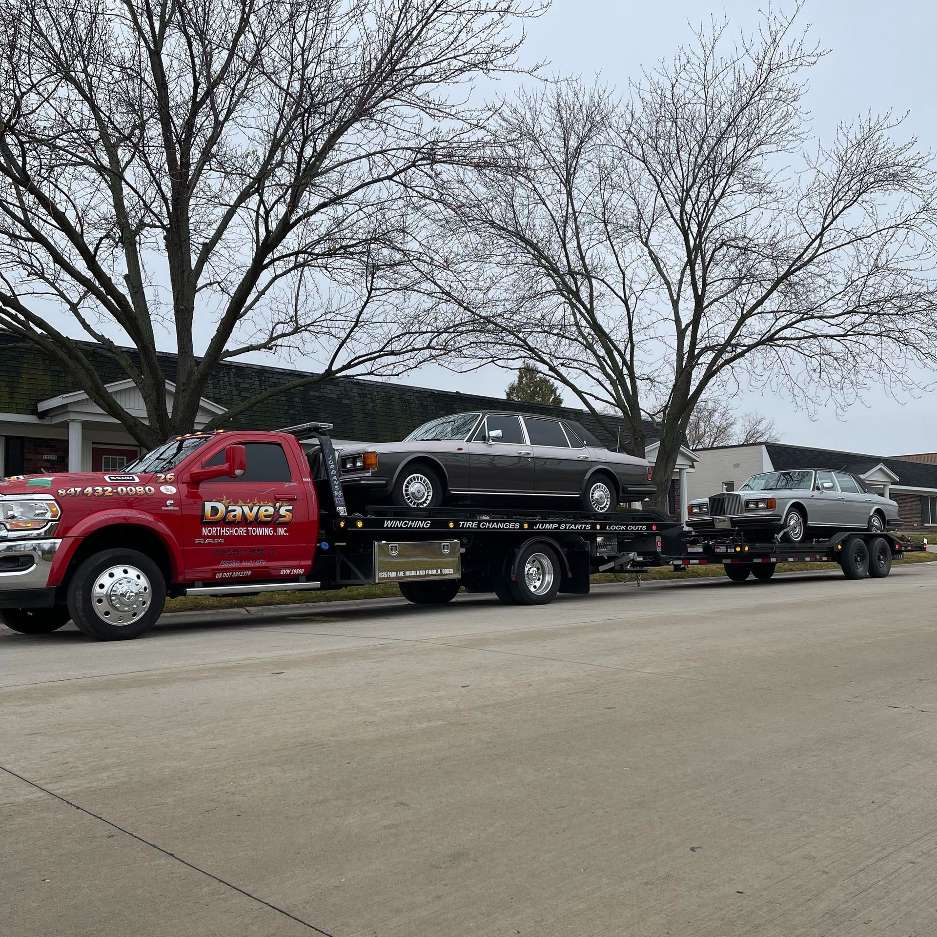 A red tow truck is carrying two cars on a trailer.