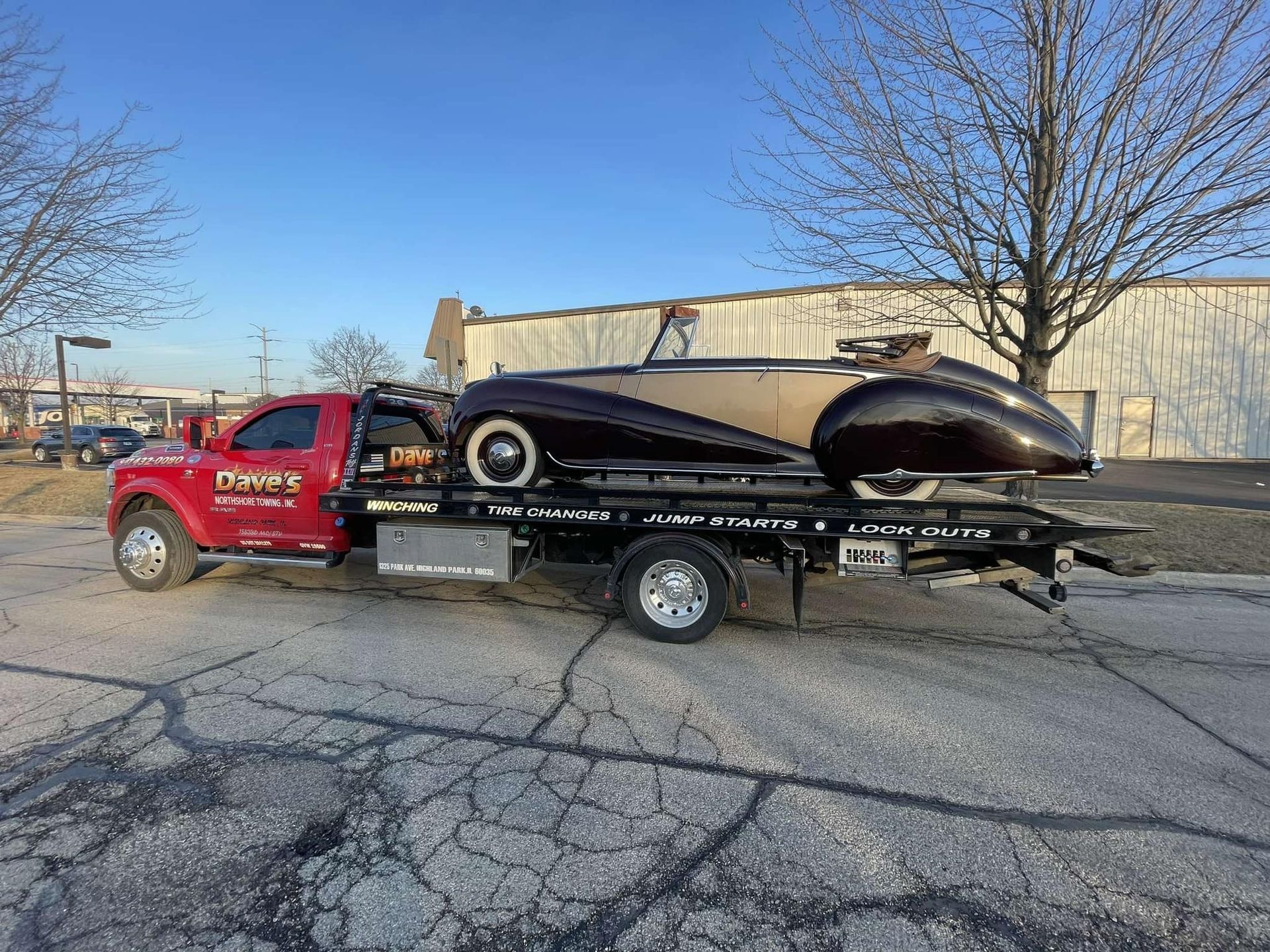 A red tow truck is carrying a black car on a trailer.