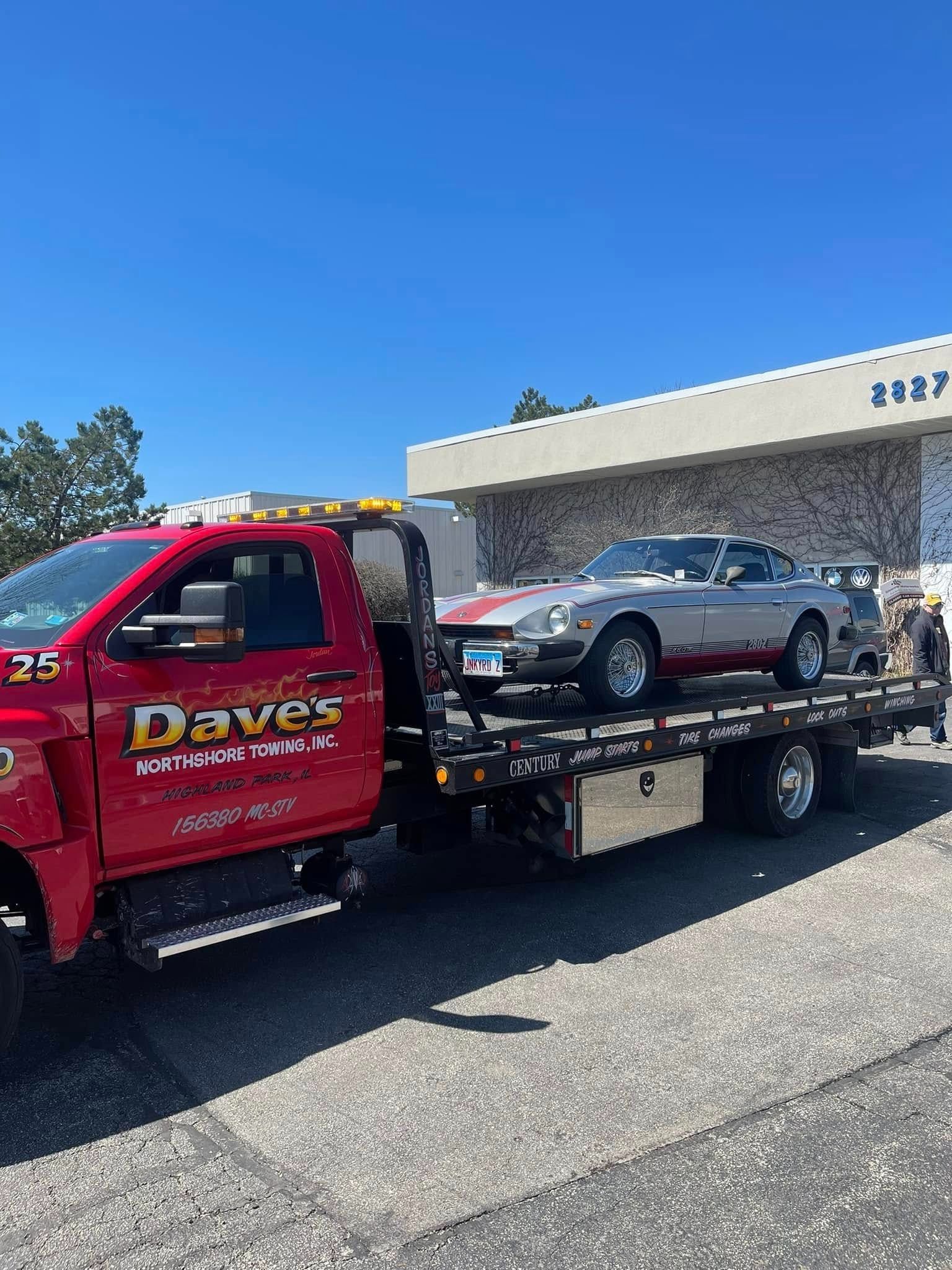 A red tow truck is towing a silver sports car.