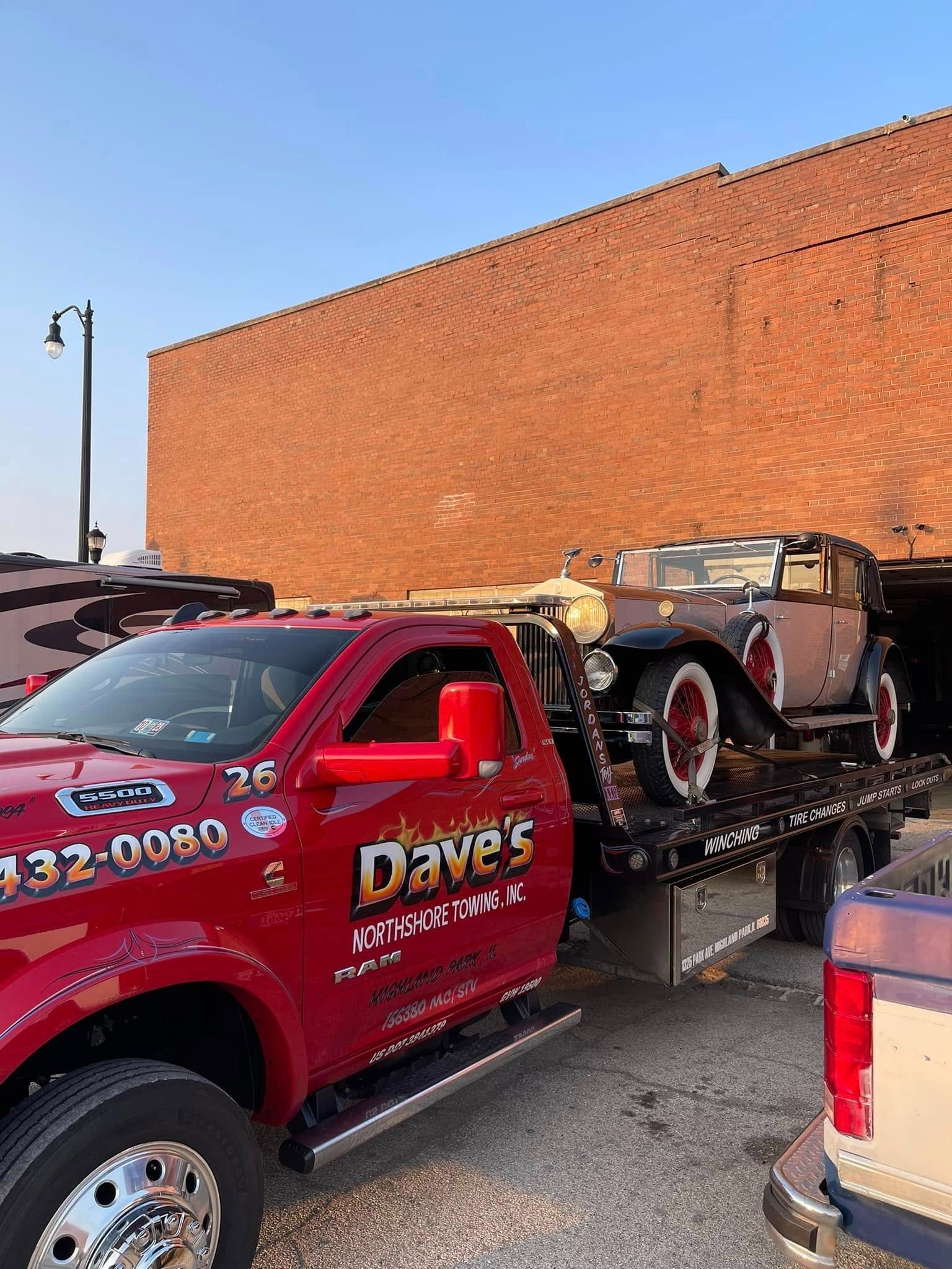 A red tow truck is carrying a car on the back of it.