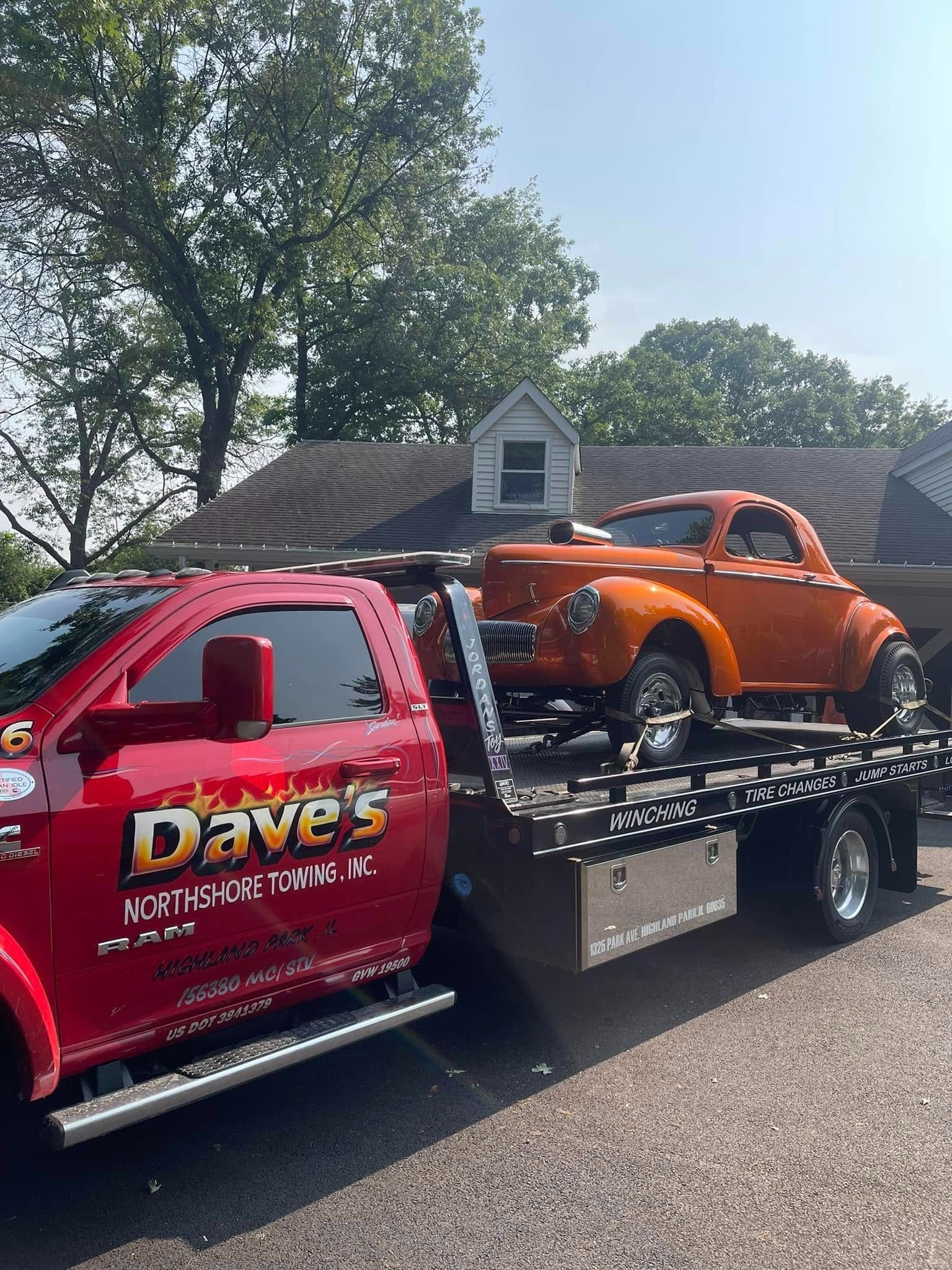A red tow truck is towing a car on a trailer.