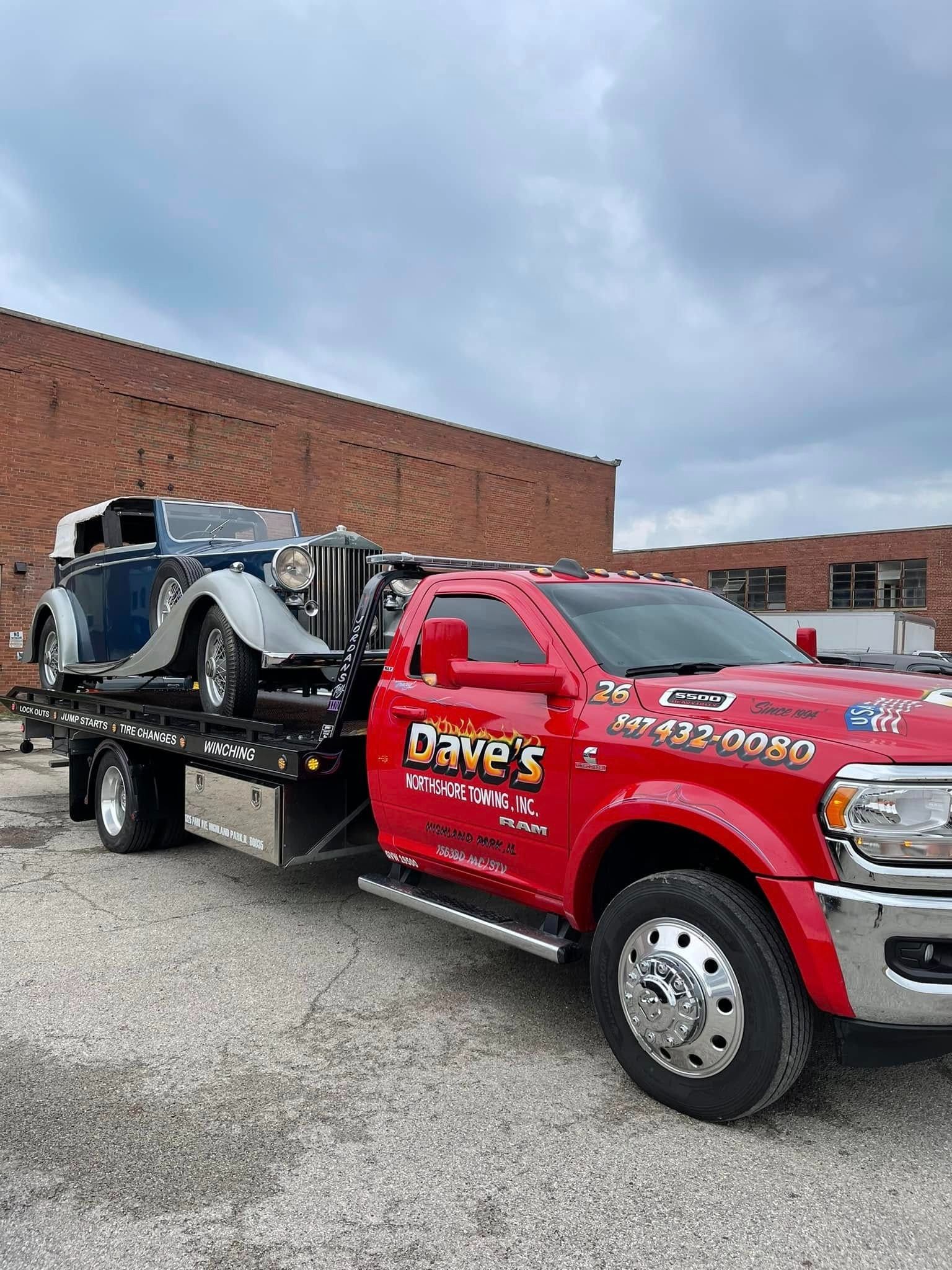 A red tow truck is towing a blue car in a parking lot.