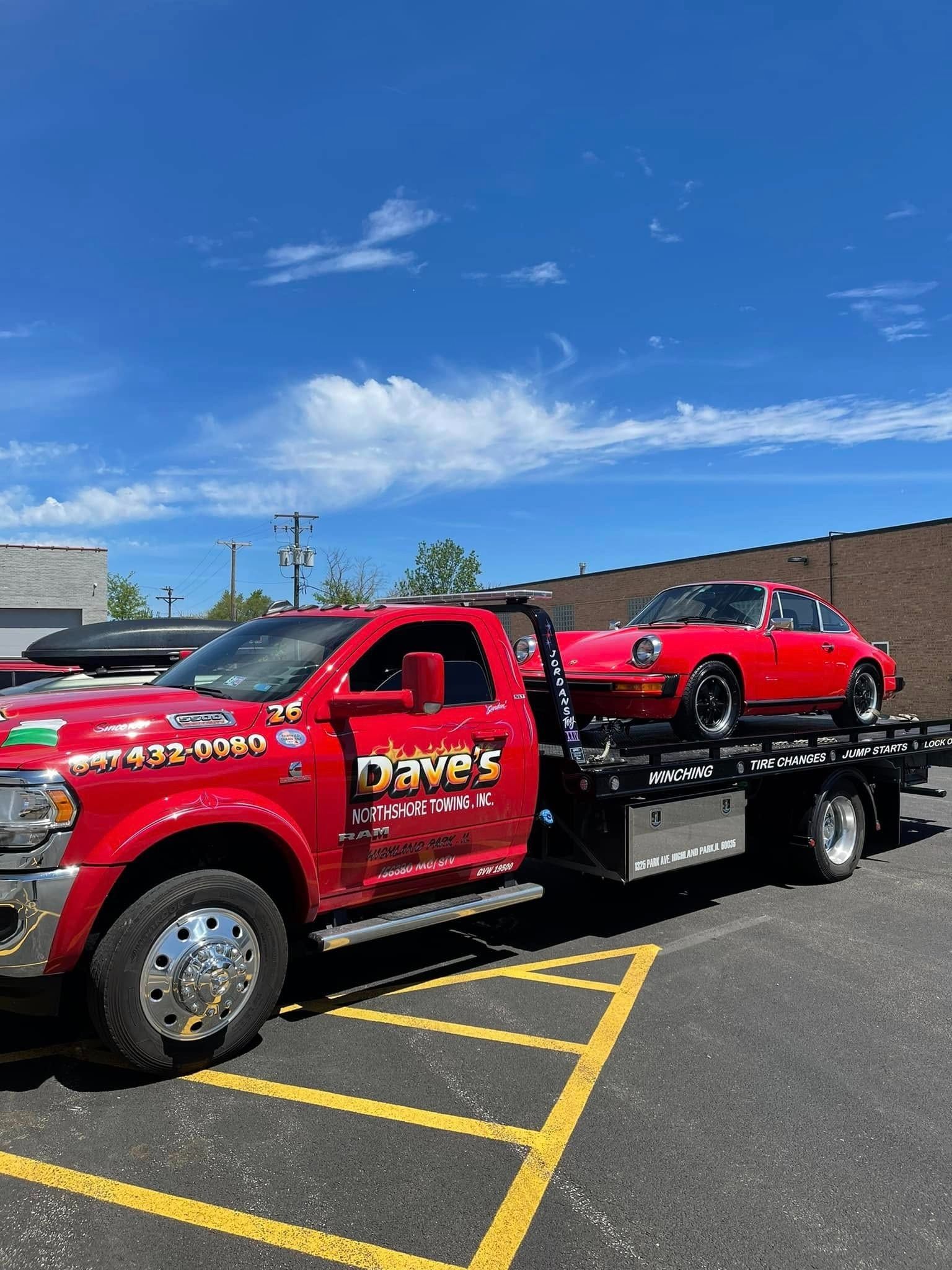 A red tow truck is towing a red car in a parking lot.