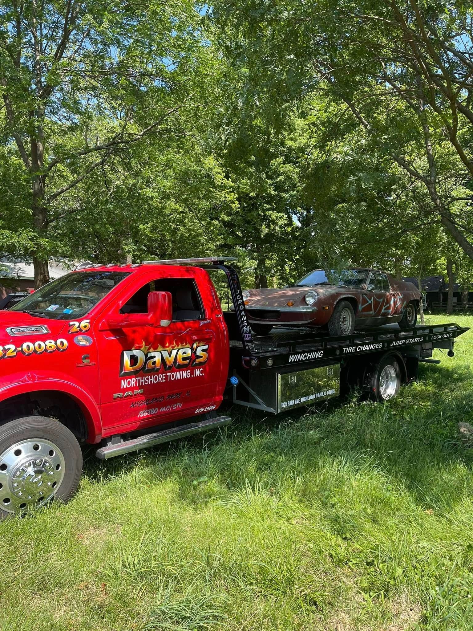 A red tow truck is carrying a car on a trailer.