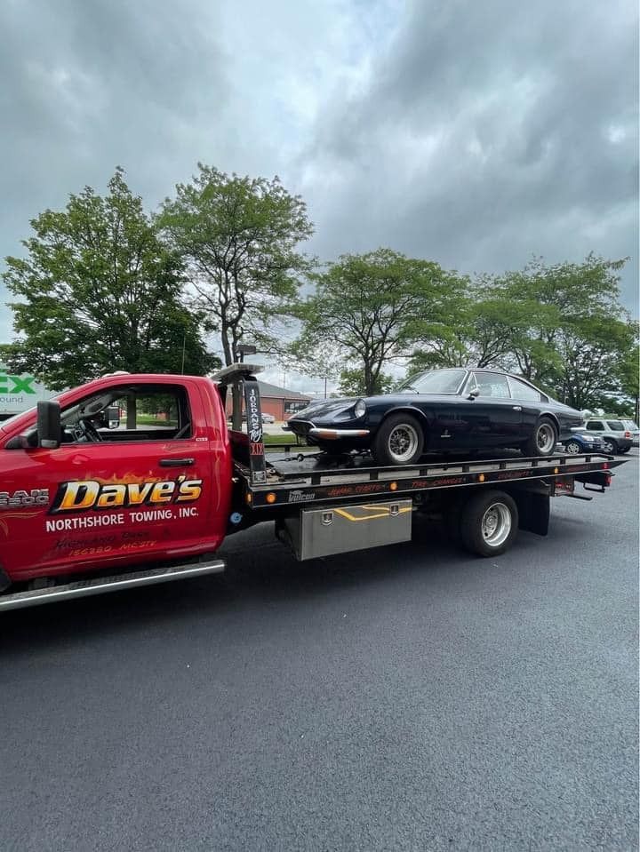 A red tow truck is towing a black car.