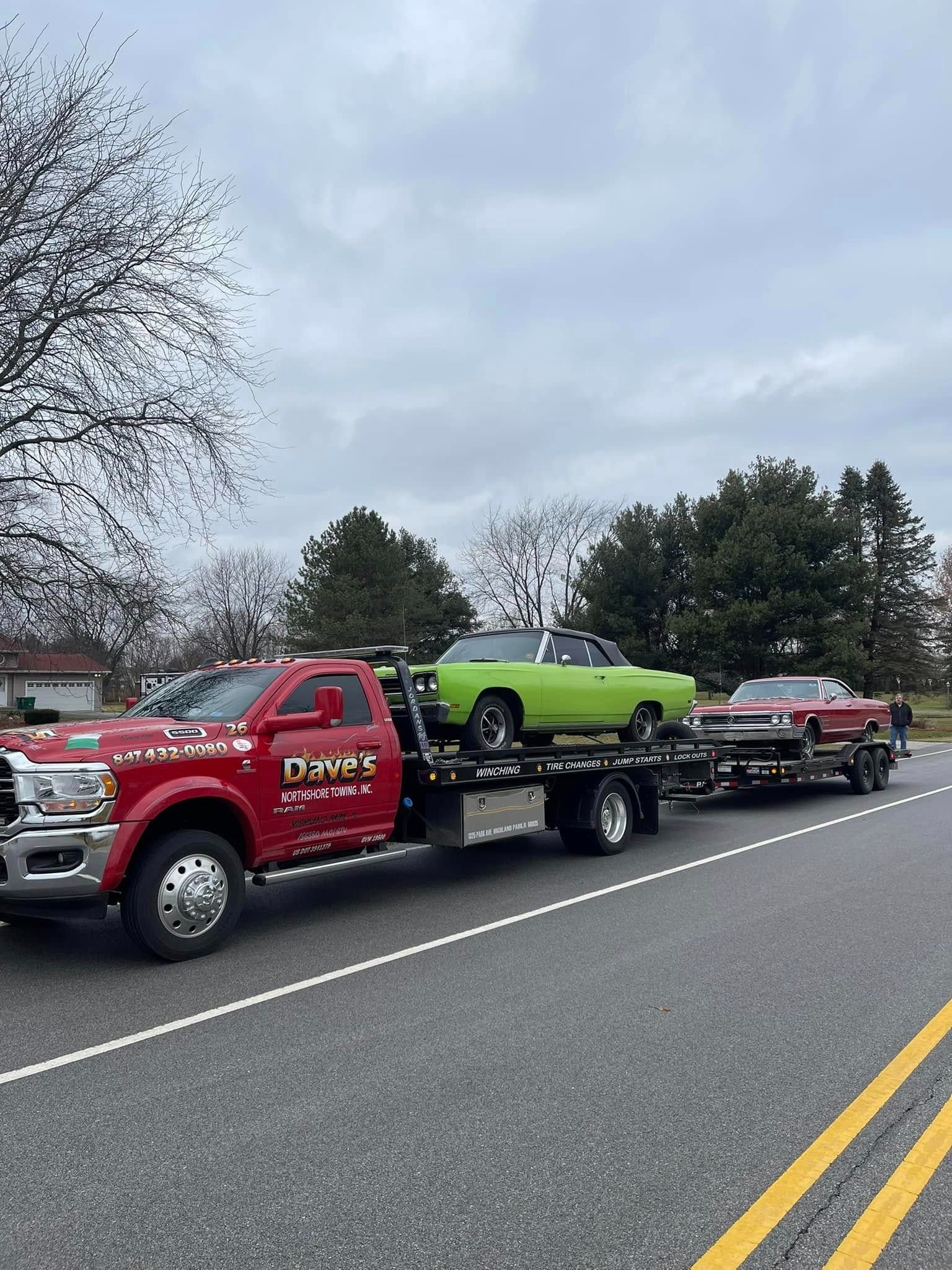 A red tow truck is towing a green car down a road.