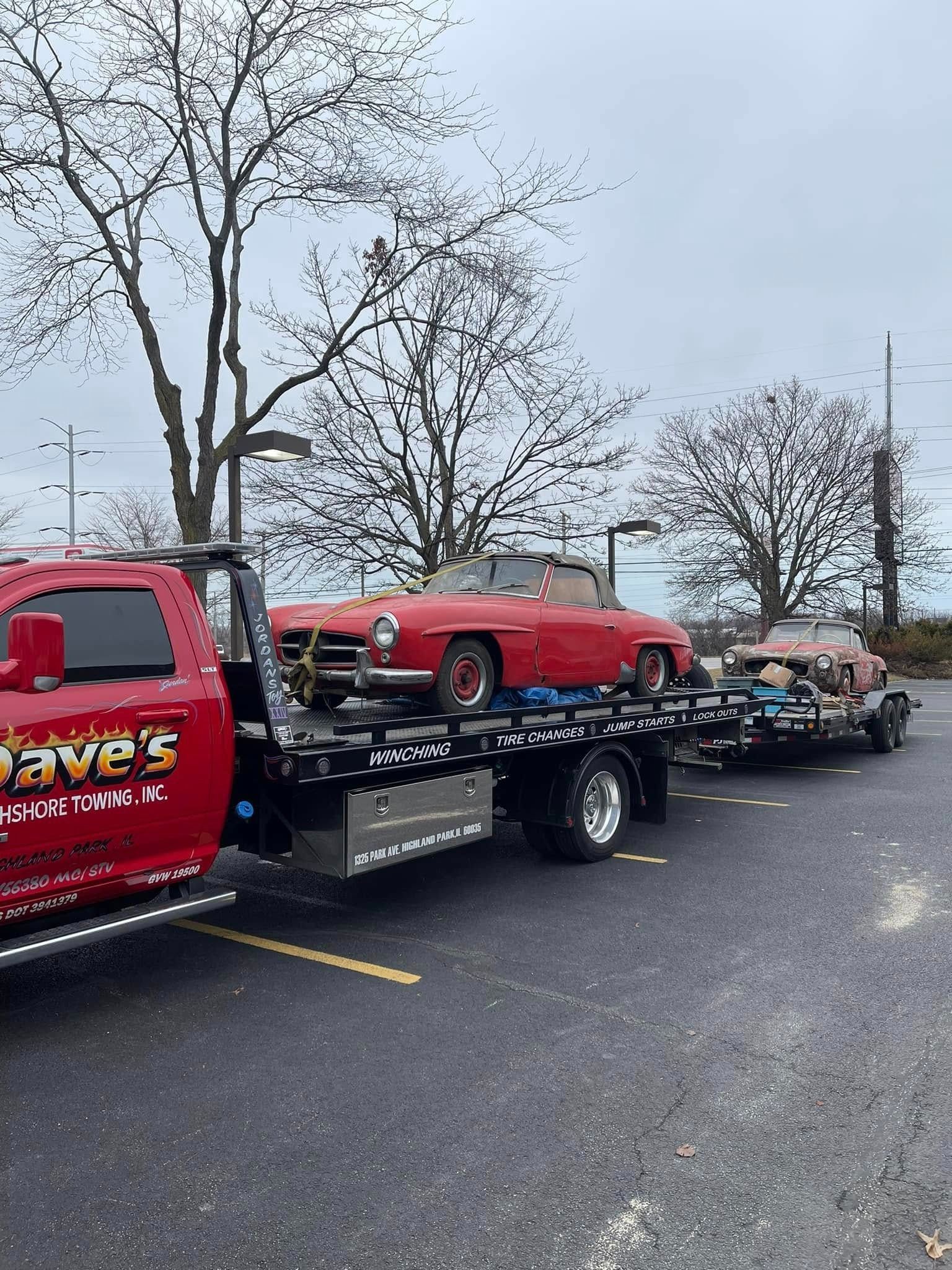 A red tow truck is towing a red sports car in a parking lot.