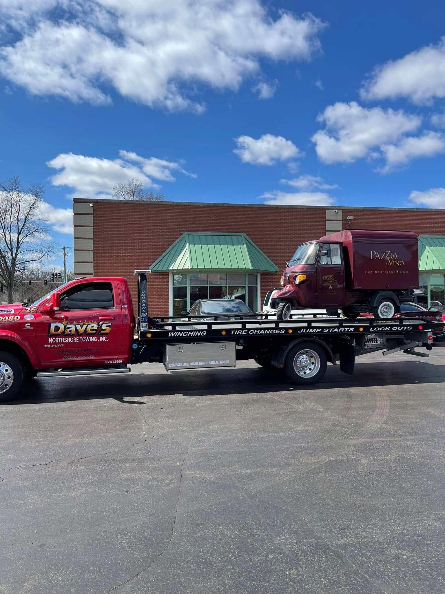 A red tow truck is towing a red truck in a parking lot.