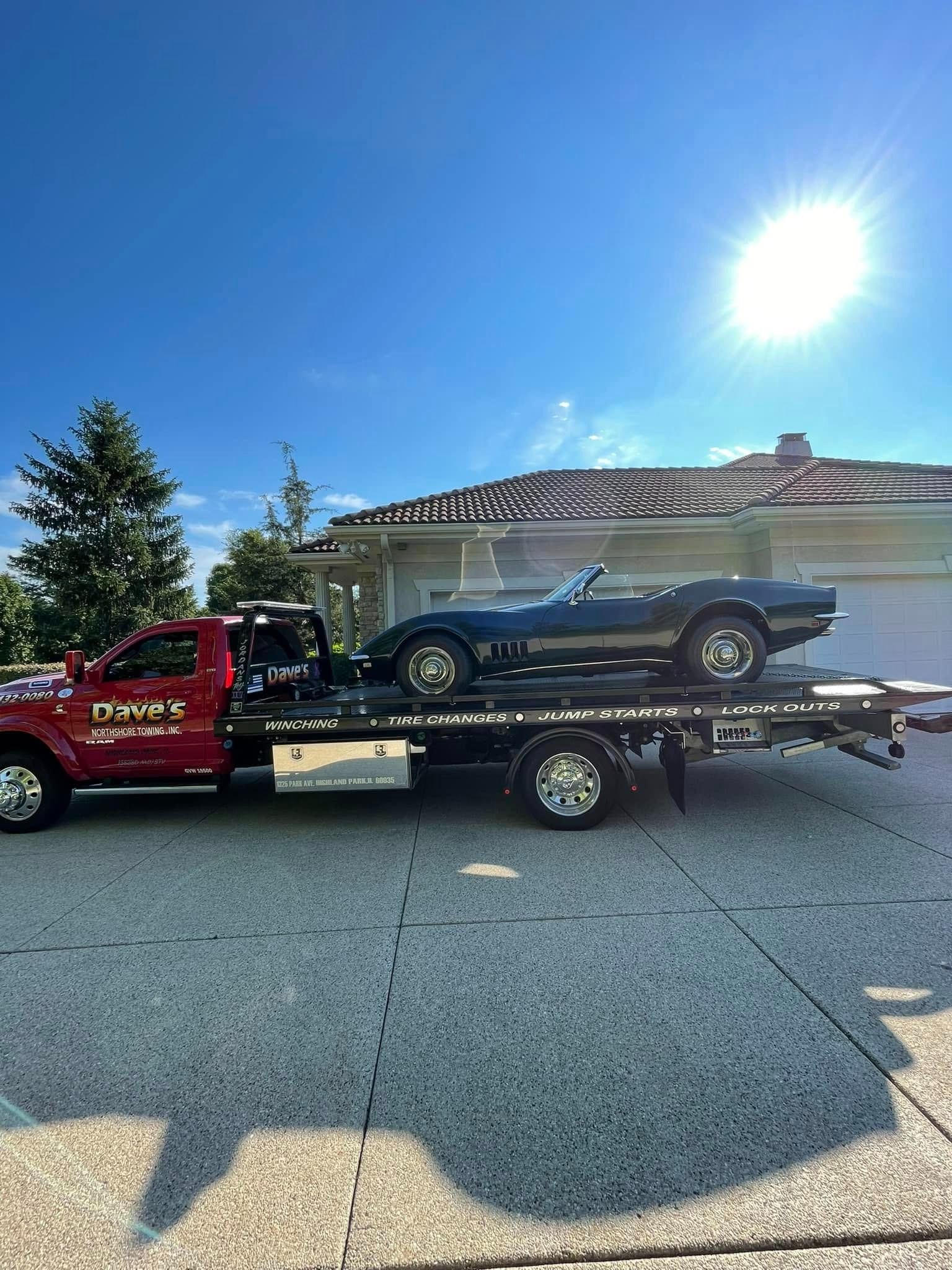 A red tow truck is towing a black car on a trailer.
