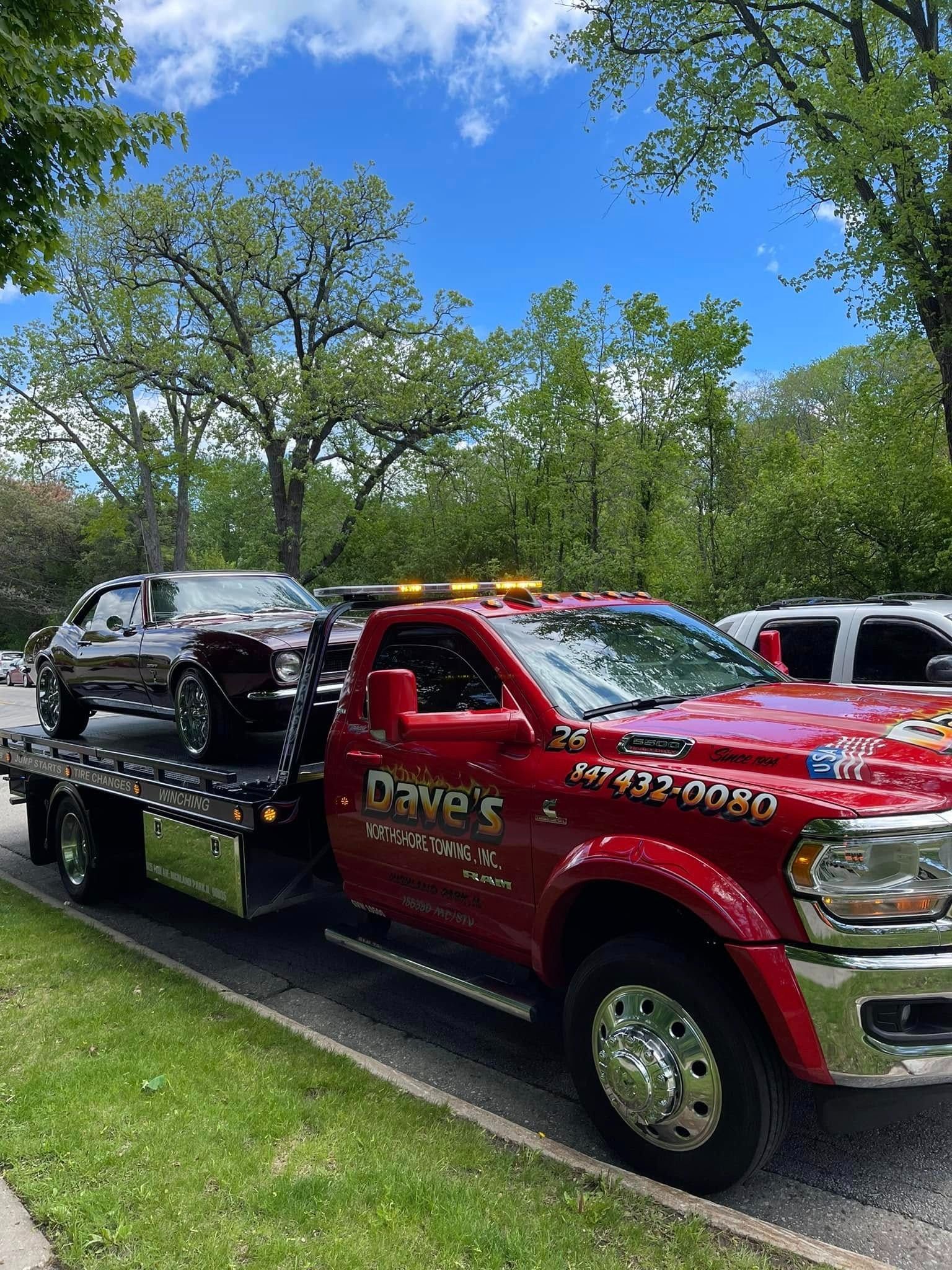 A red tow truck with a car on the back is parked on the side of the road.