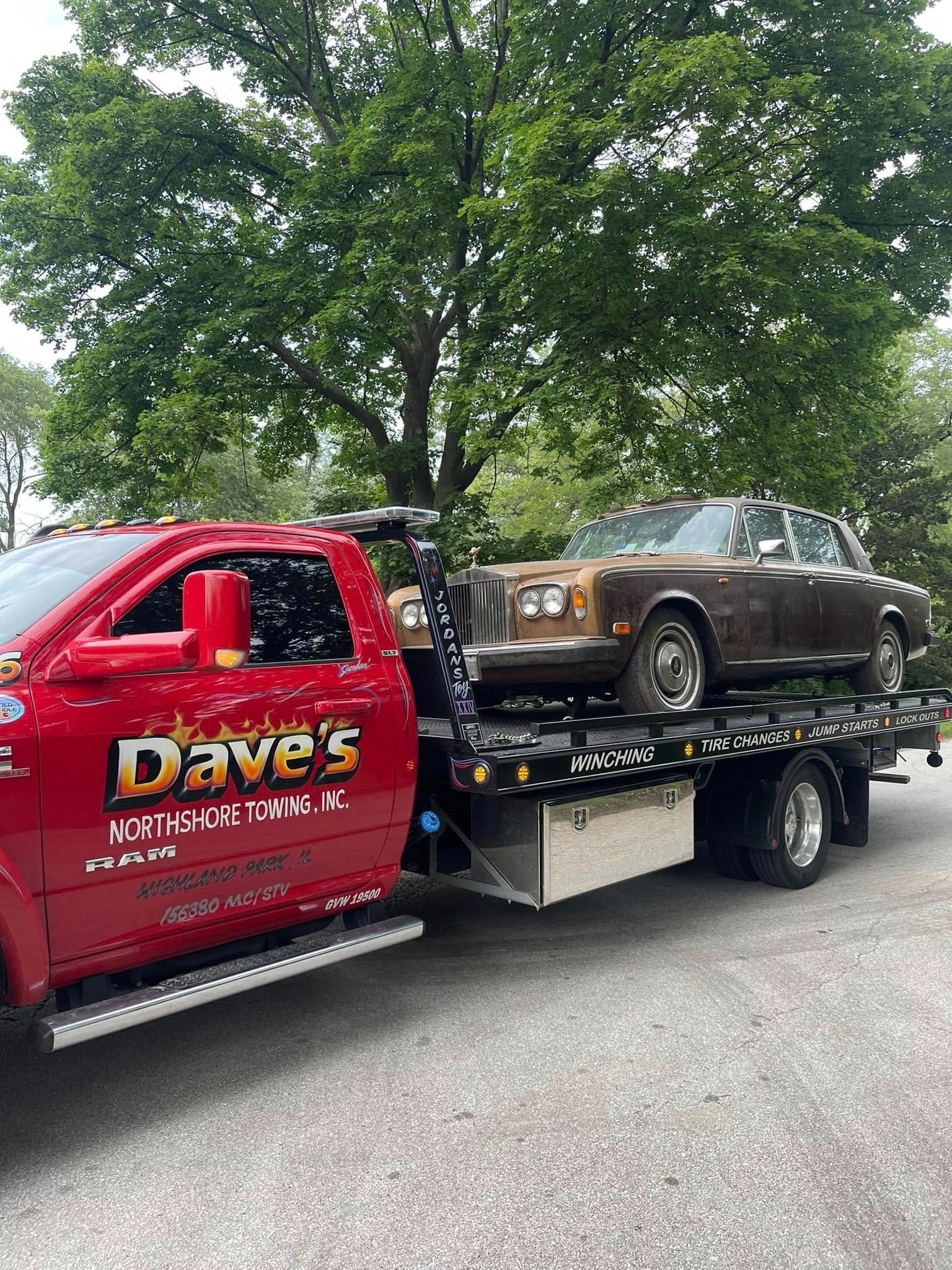A red tow truck is towing a brown car.