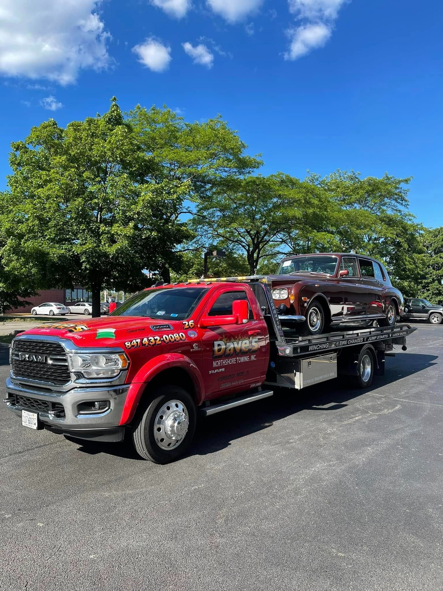 A red tow truck is towing a car in a parking lot.