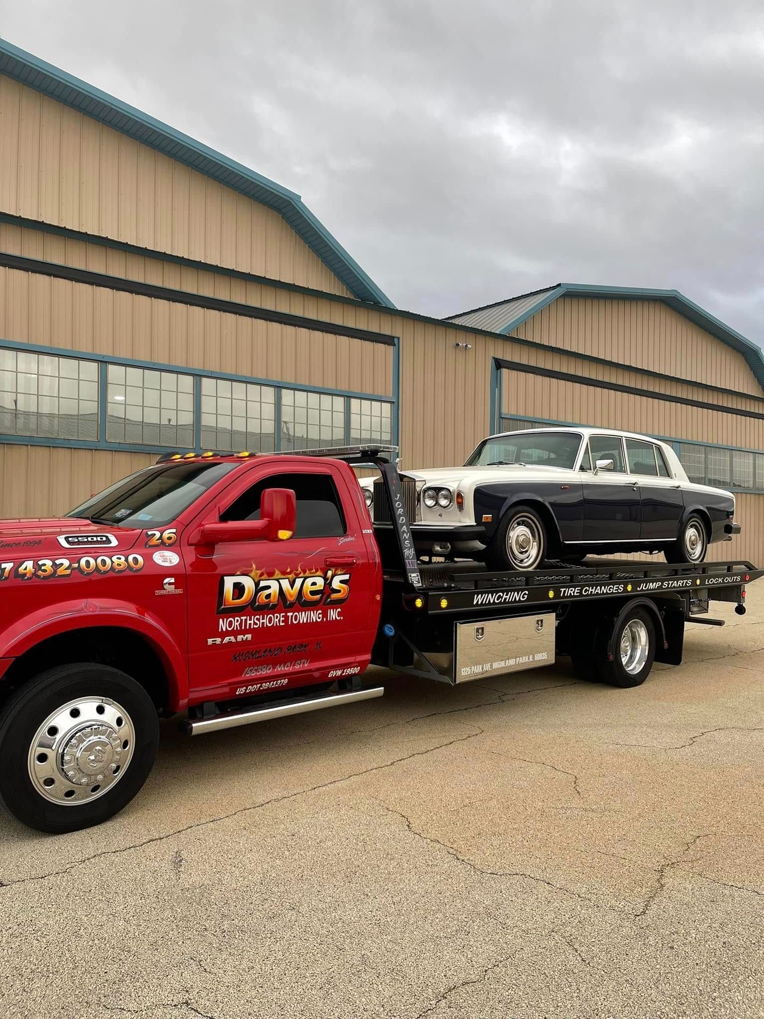 A red tow truck is towing a black and white car.